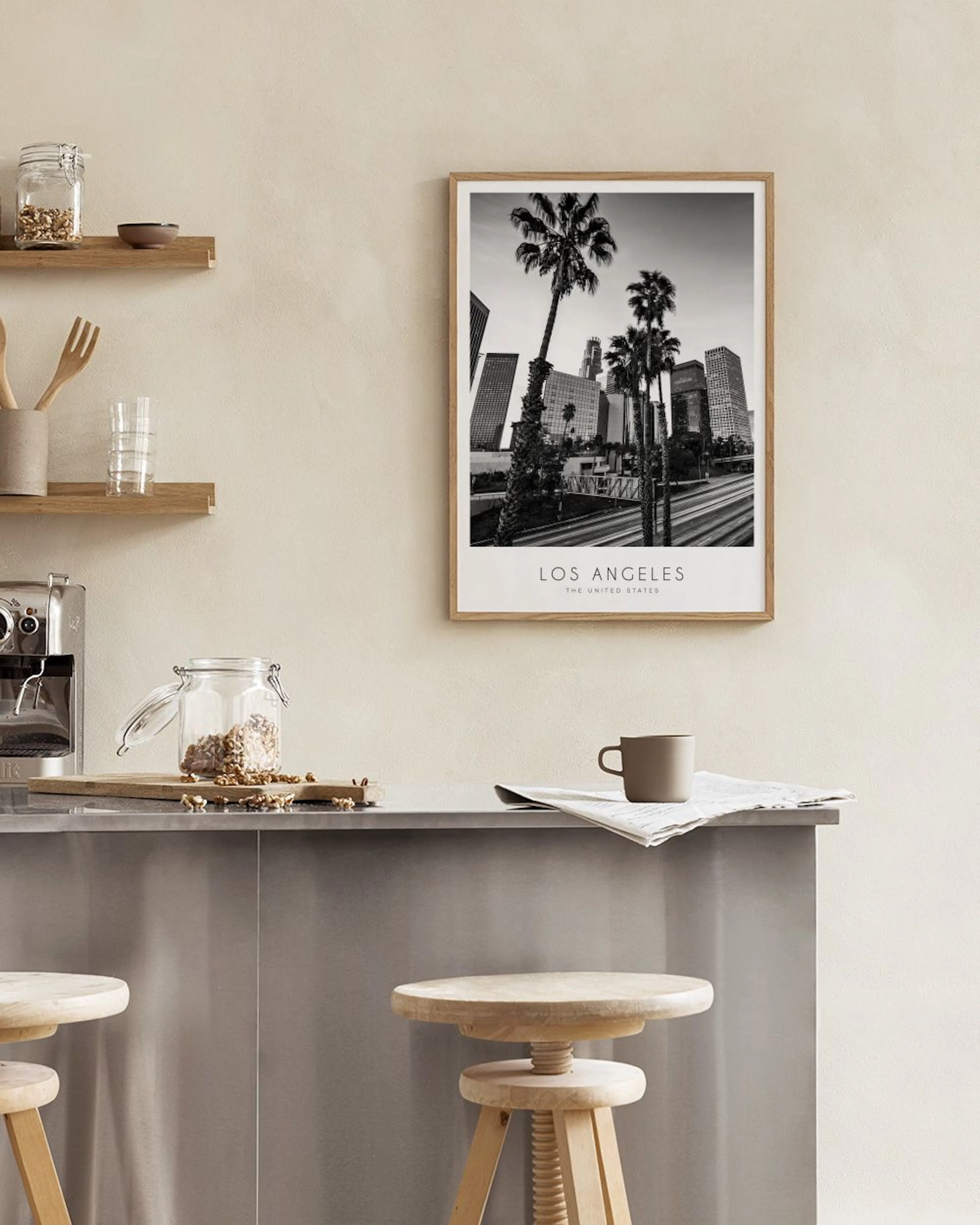 Black and white cityscape print of Los Angeles with palm trees and tall buildings, hanging above a wooden bench with decor.