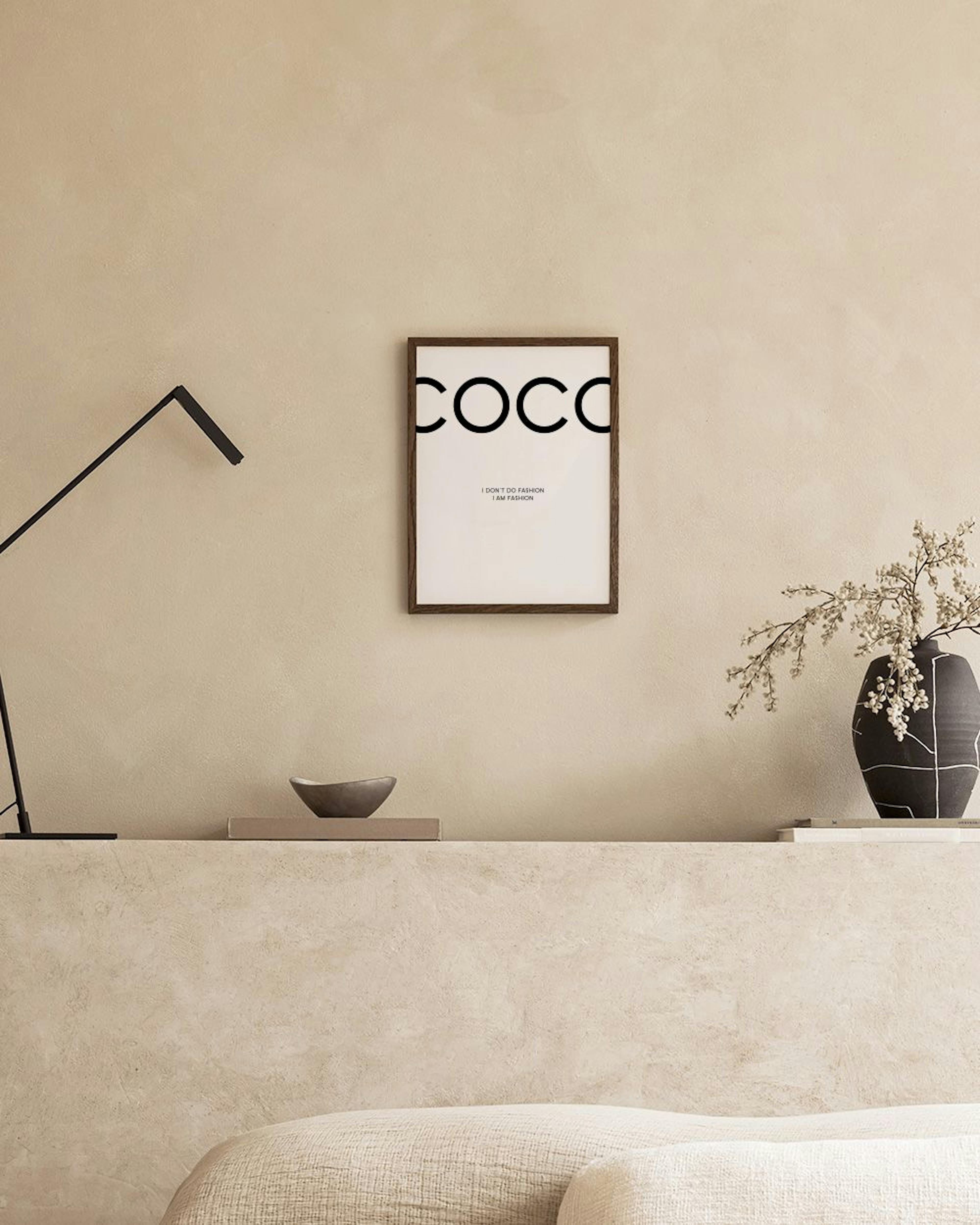 Schwarz-weißes Poster mit dem Wort COCO und dem Zitat I DONT DO FASHION I AM FASHION, über einem Regal mit Büchern und Deko.