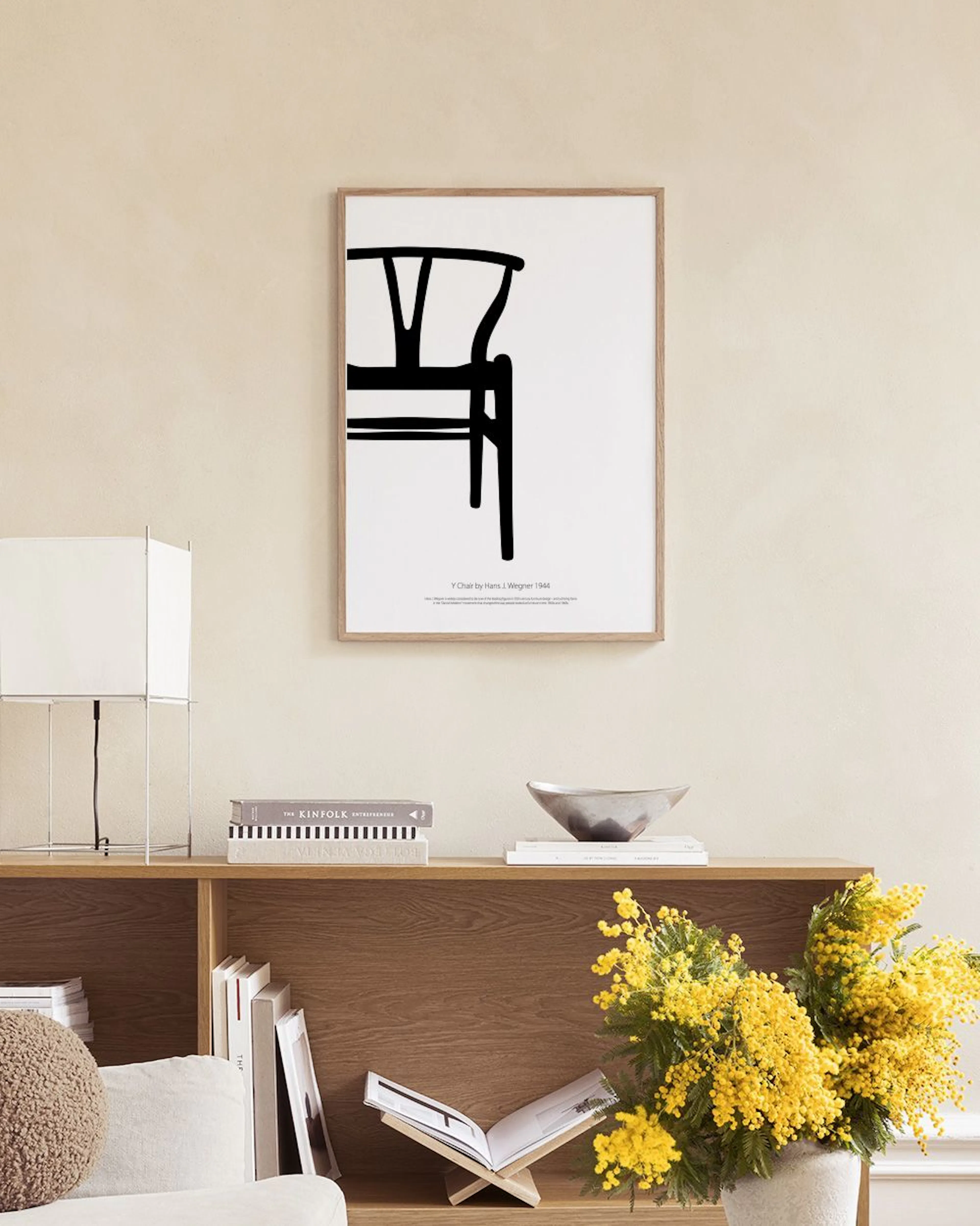 Dos pósters de diseño minimalista, uno con una & y otro con una silla, apoyados sobre un aparador blanco con jarrones y libros.