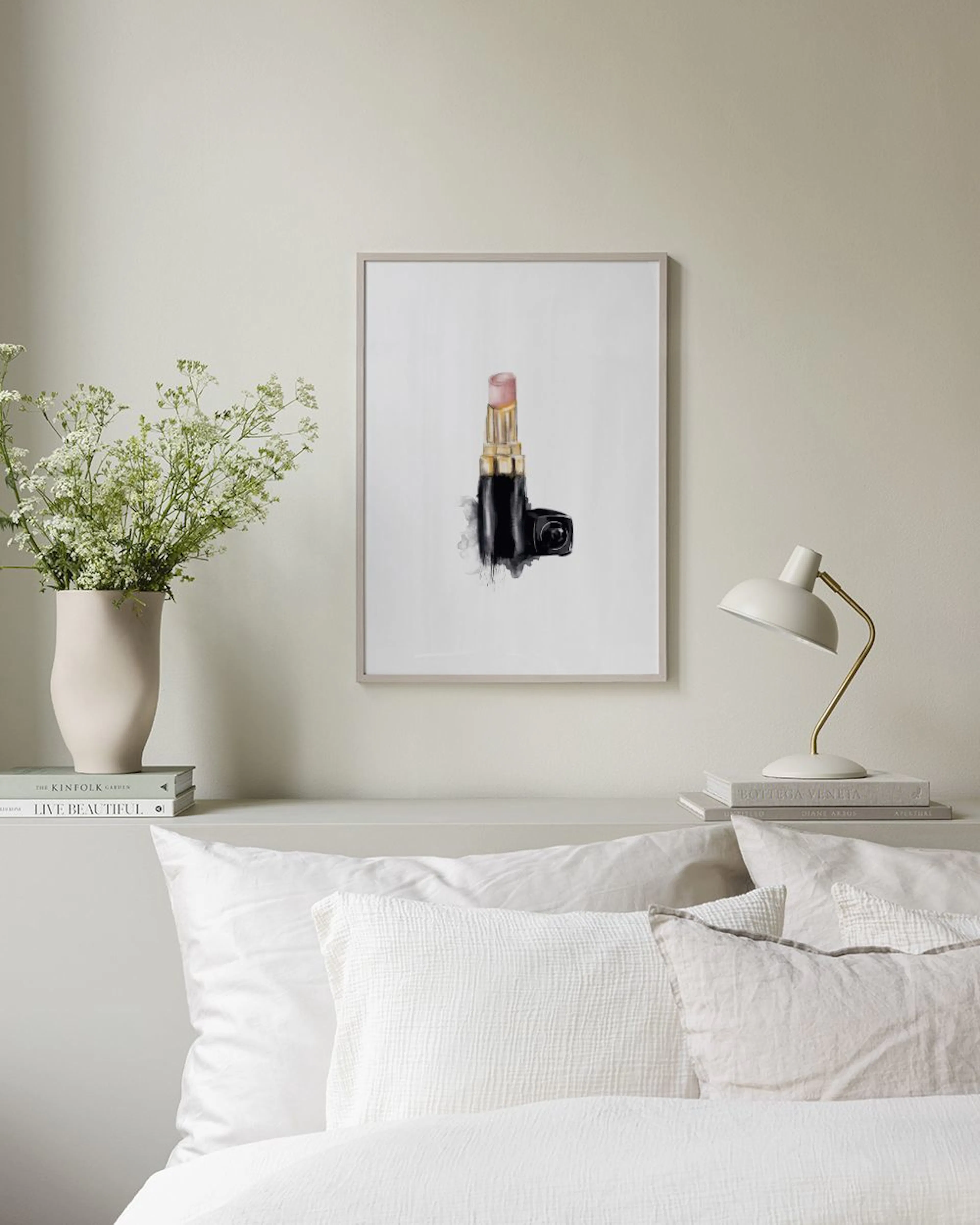 Poster van een roze lippenstift met zwarte en gouden details, staand op een zwarte plank met kaarsen en decoratie.