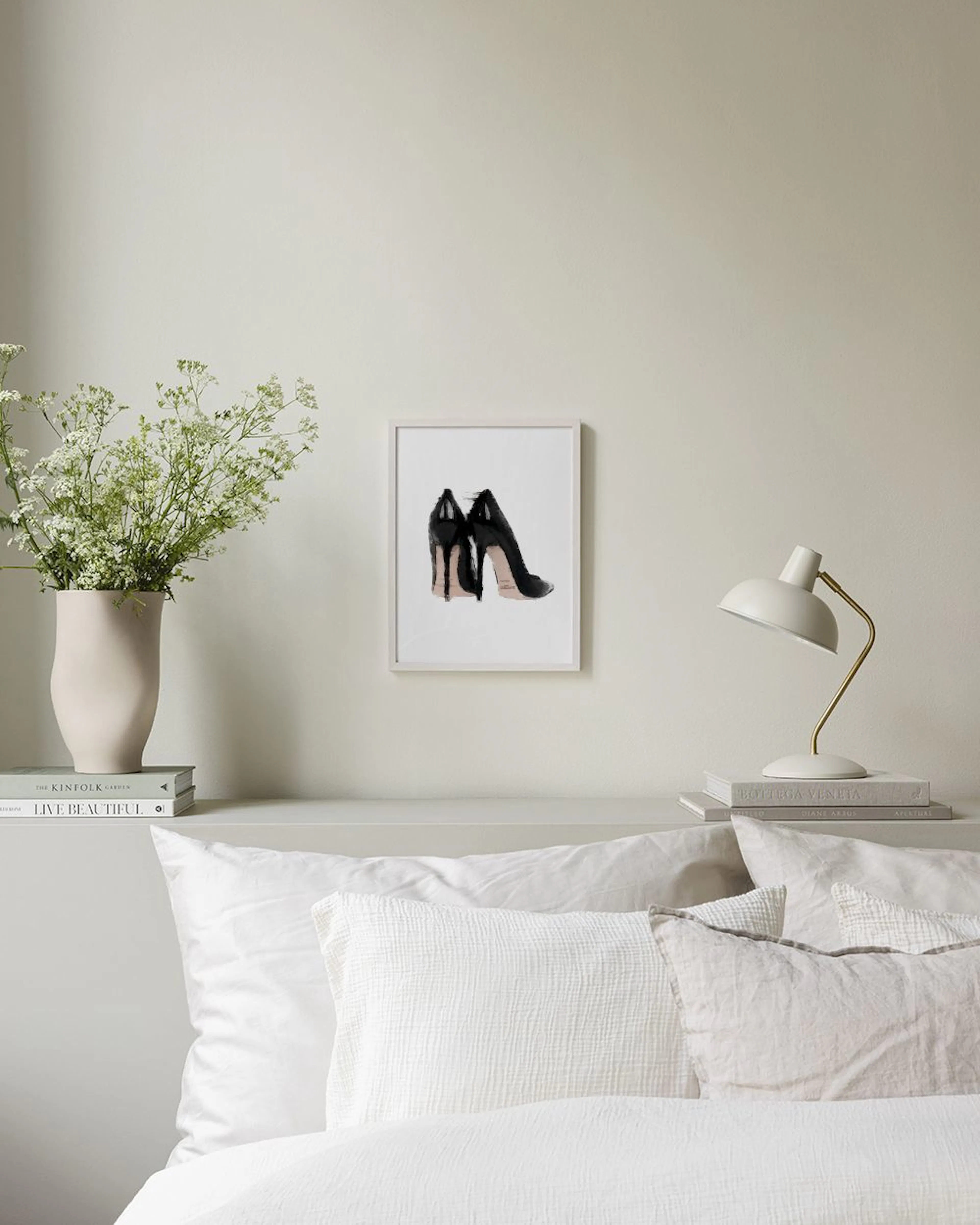 A fashion print of black high heels with a beige sole, displayed in a stylish room with a gold mirror and pink roses.
