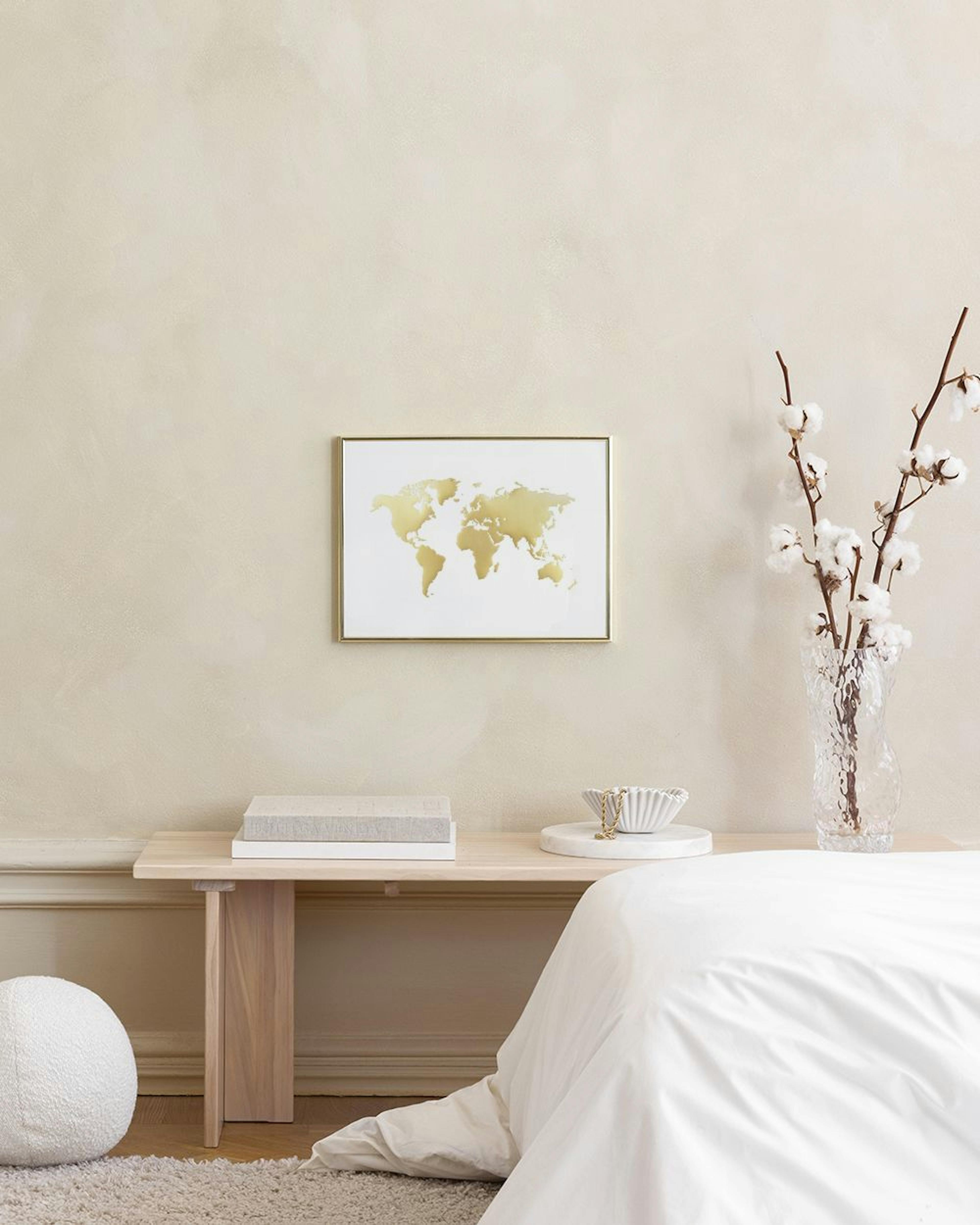 Affiche carte du monde dorée sur fond blanc, suspendue au-dessus dune table noire dans un salon moderne.