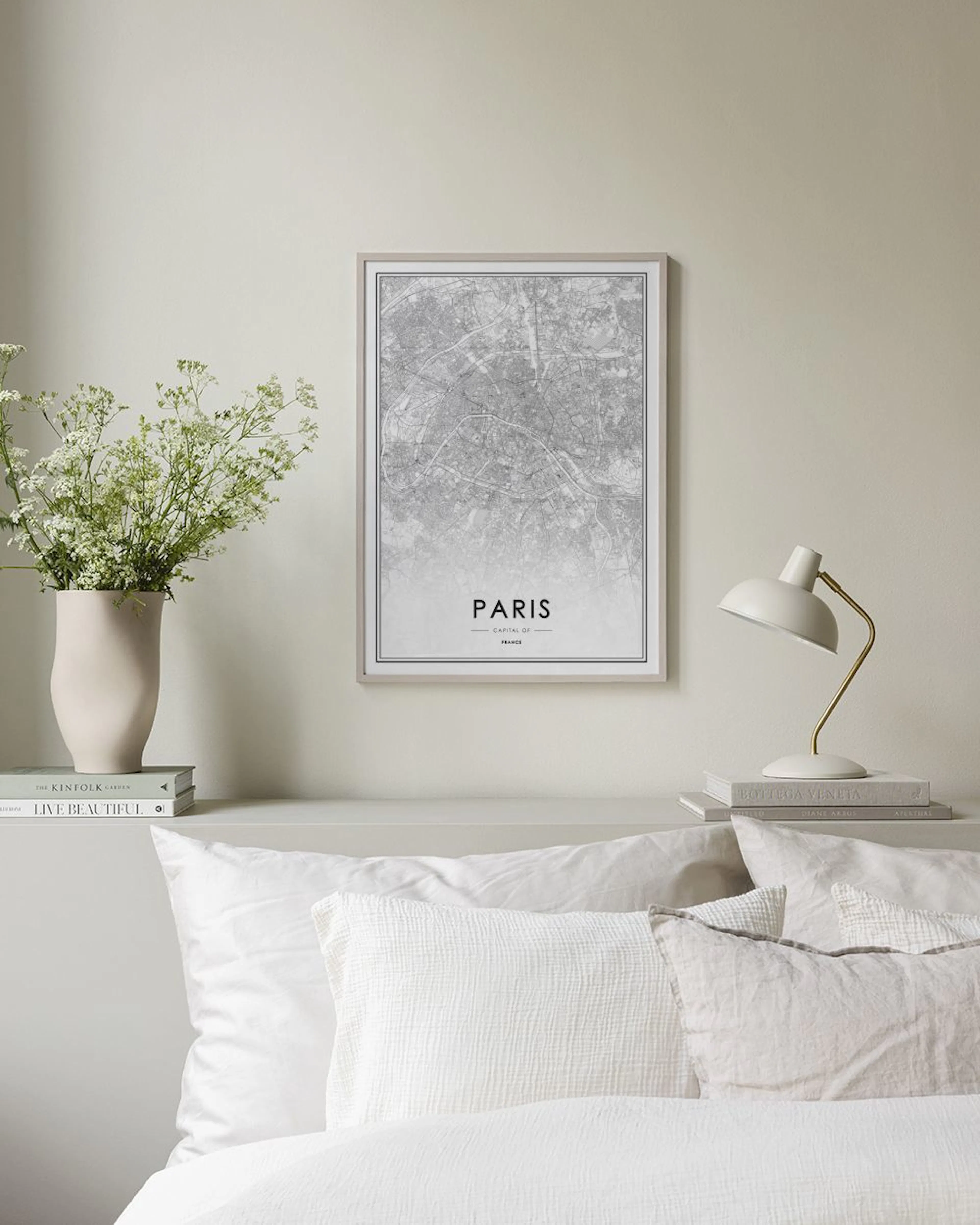 Plakat med kart over Paris i svart-hvitt, stående på en hvit hylle med en kaktus og lysestake.