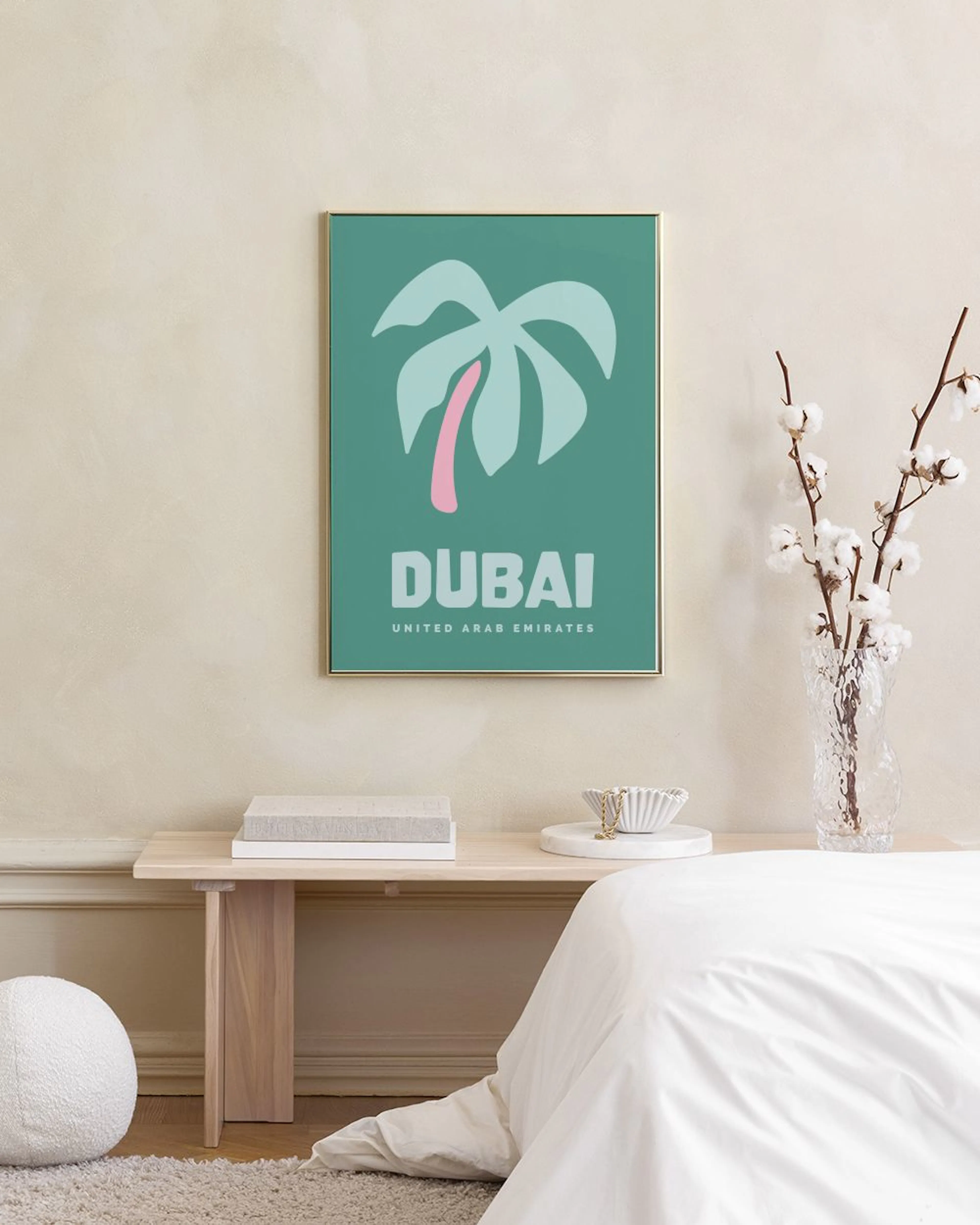 Plakat med hvid palme og lyserød stamme på mintgrøn baggrund, der siger DUBAI, hængende over et træskrivebord.
