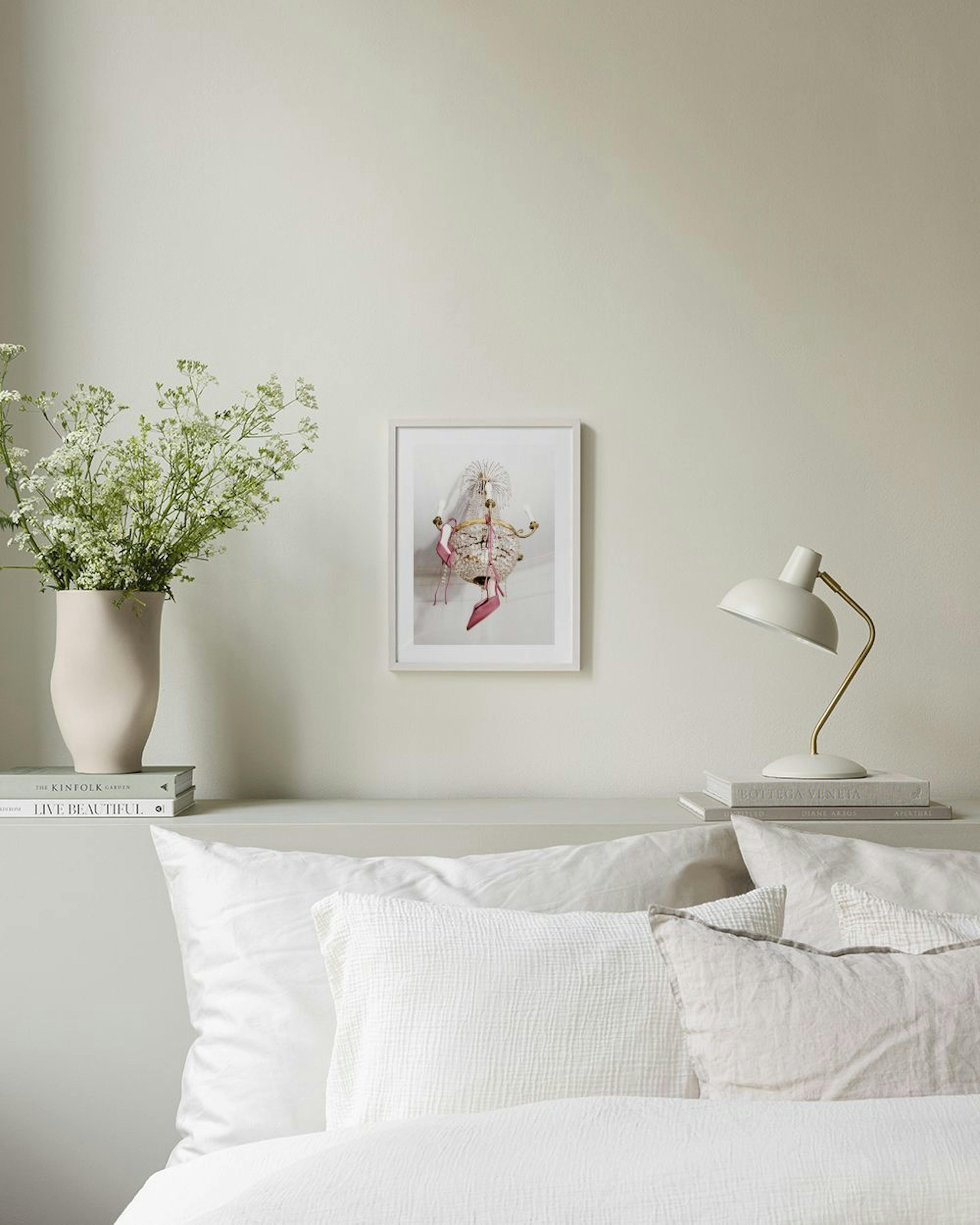 A print of pink high heels hanging from a crystal chandelier, displayed above a pink velvet bench in a room.