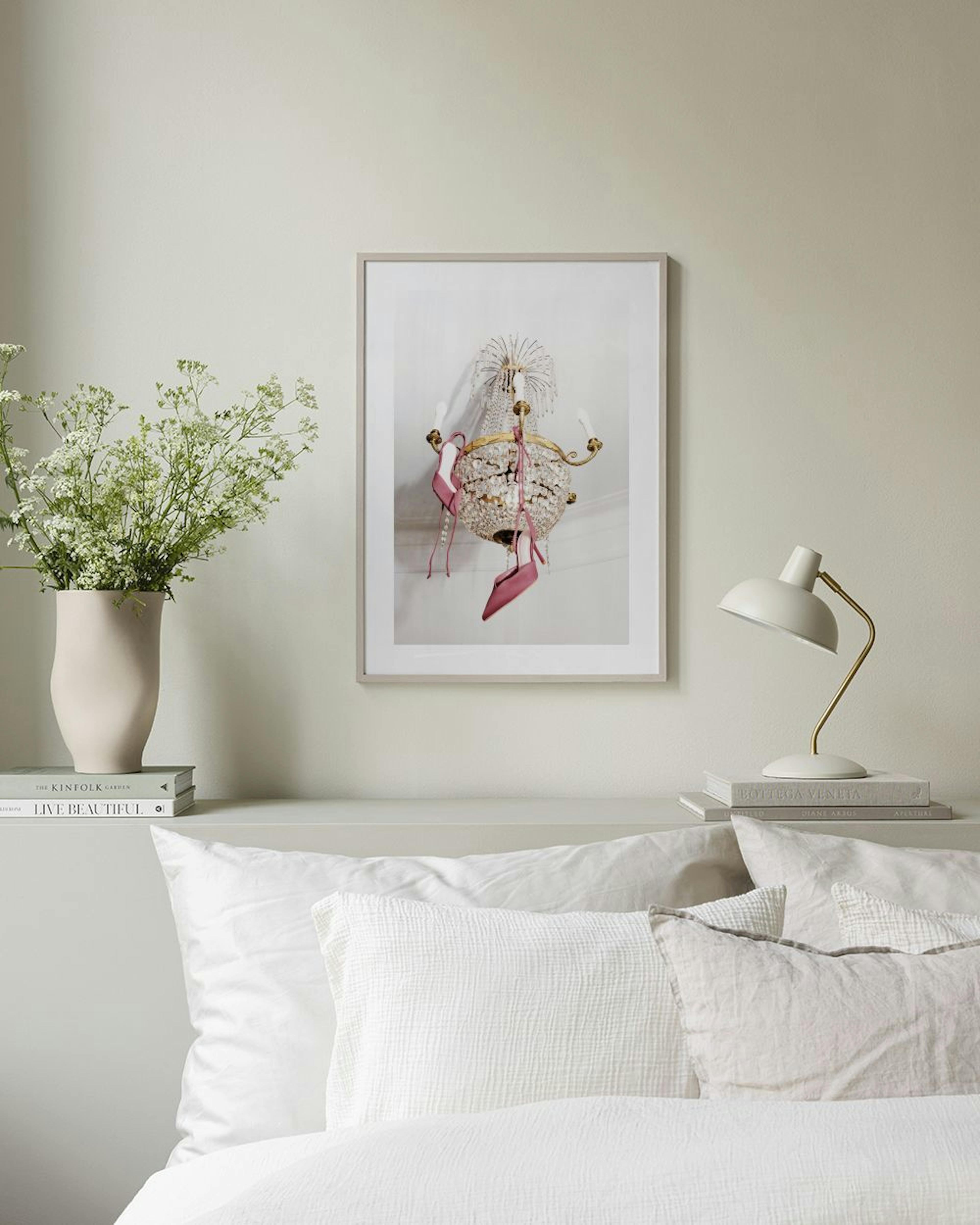 Poster con un candelabro di cristallo dorato e scarpe rosa appese, esposto sopra una panca rosa in velluto.