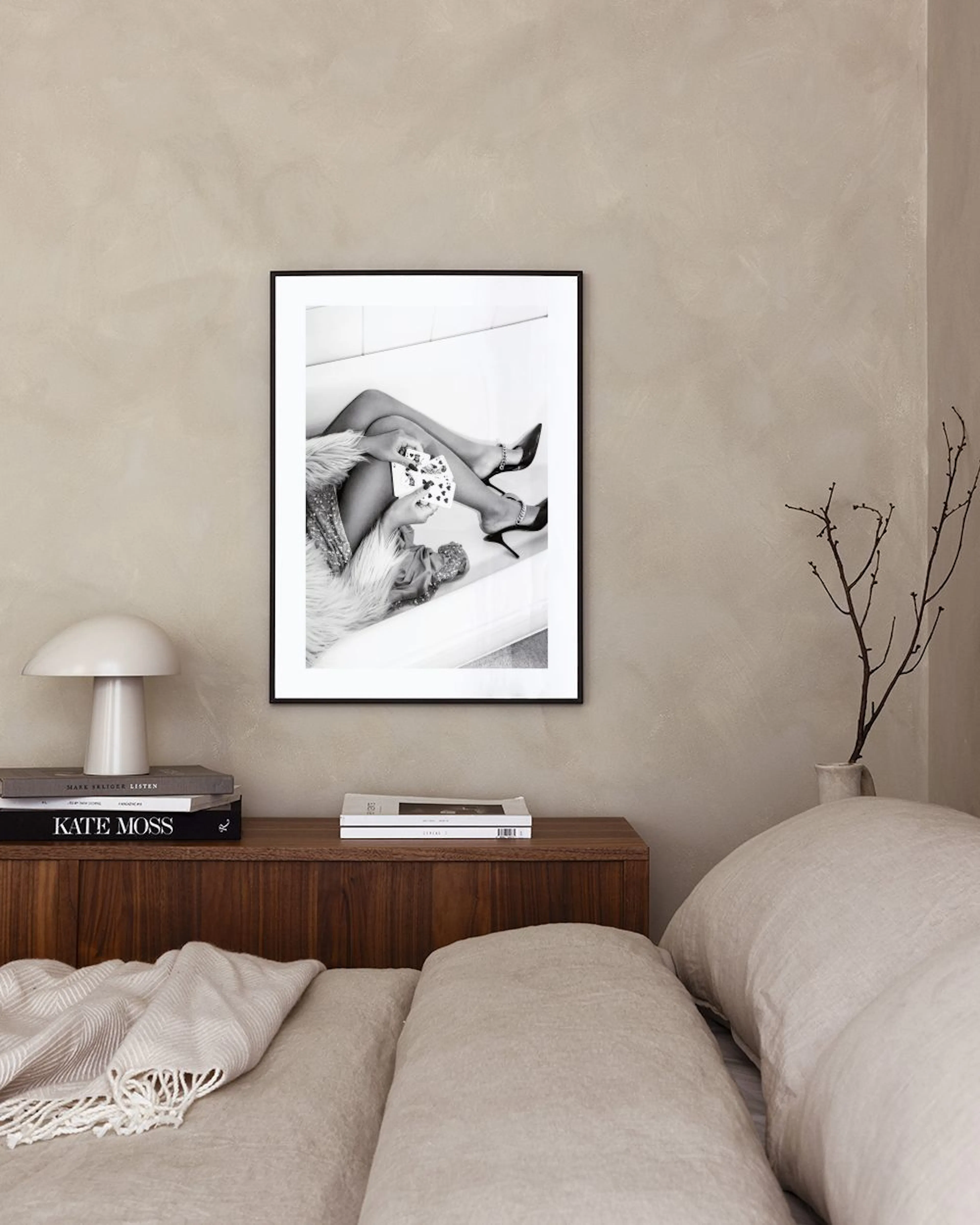 Black and white print of a woman in high heels and fur holding playing cards, hanging above a pink velvet bench.