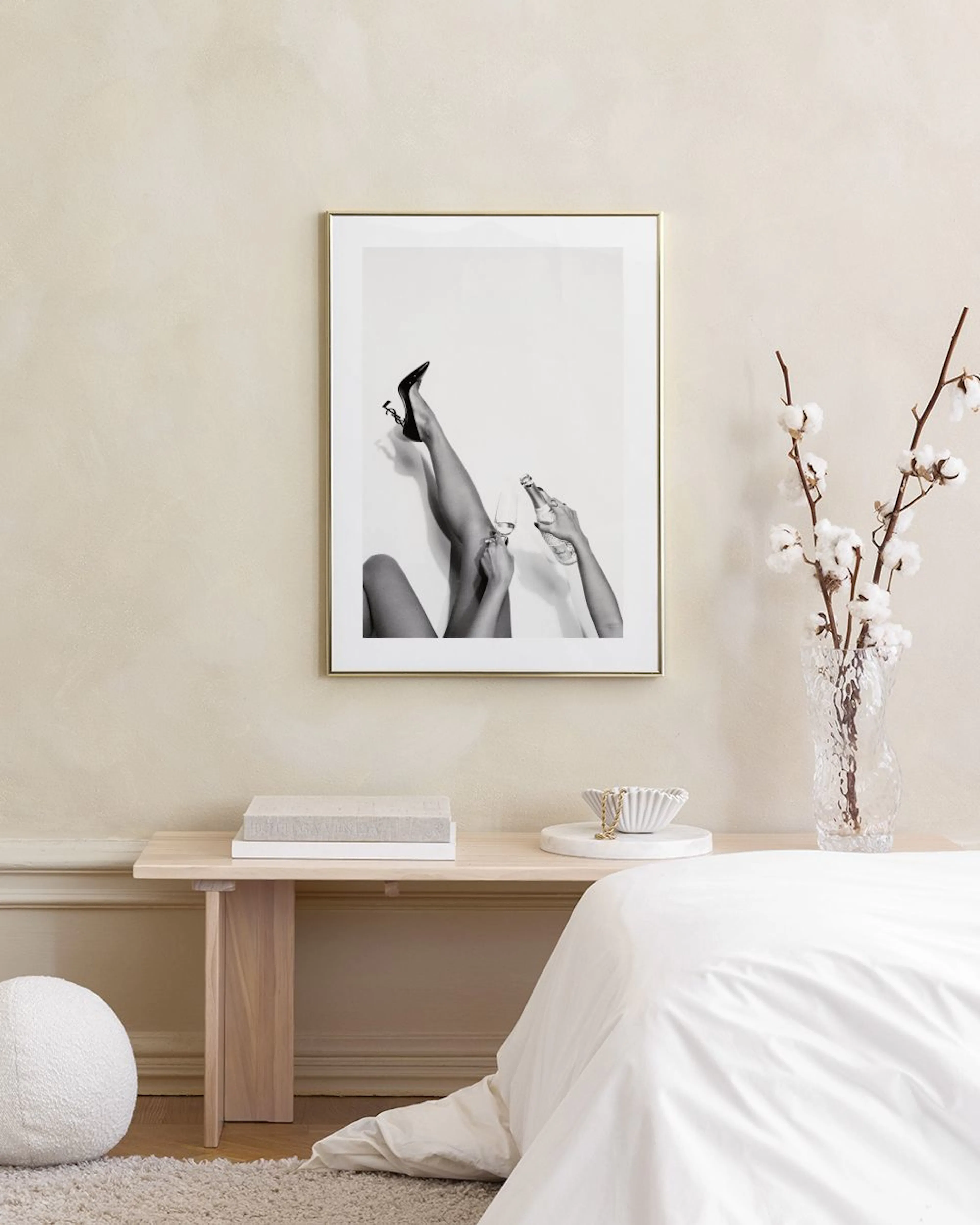 A black and white print of a womans legs in a high heel and hands holding a drink, hanging above a red sofa.