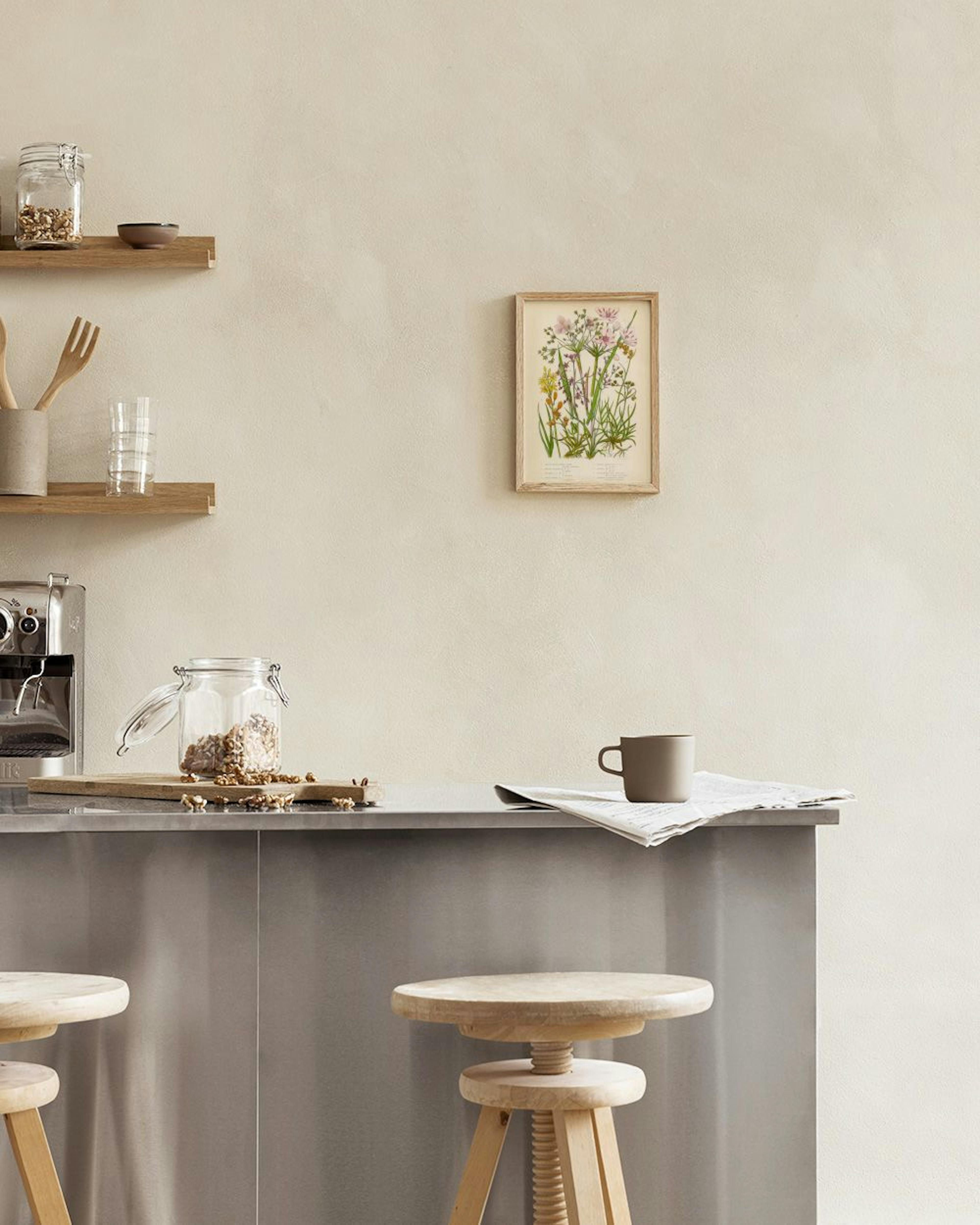 Botanical print with pink and yellow flowers on a light background, hanging on a white wall above a stool with books.