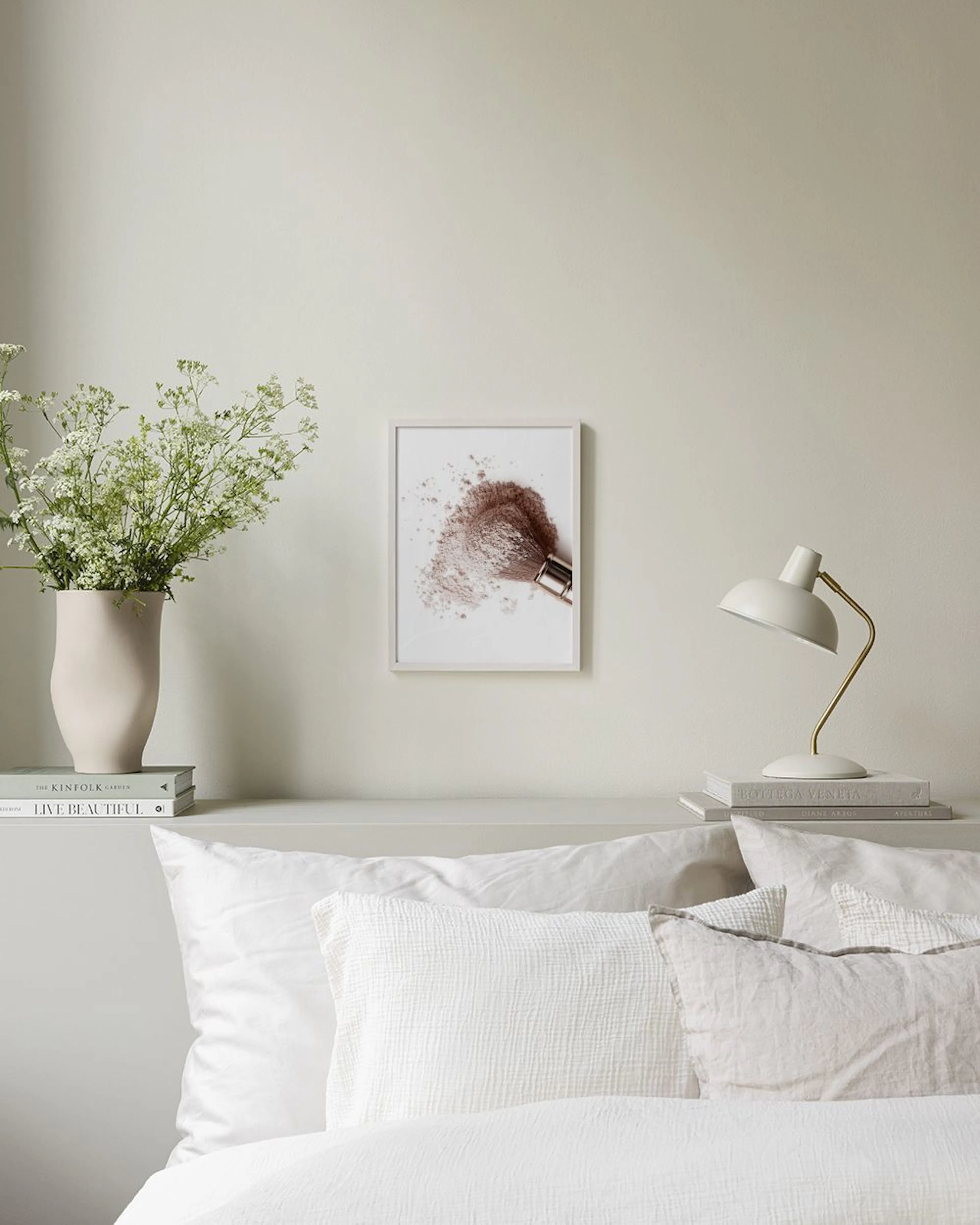 Poster met een make-upkwast in bronspoeder, hangend boven boeken en decoratie op een zwarte plank.