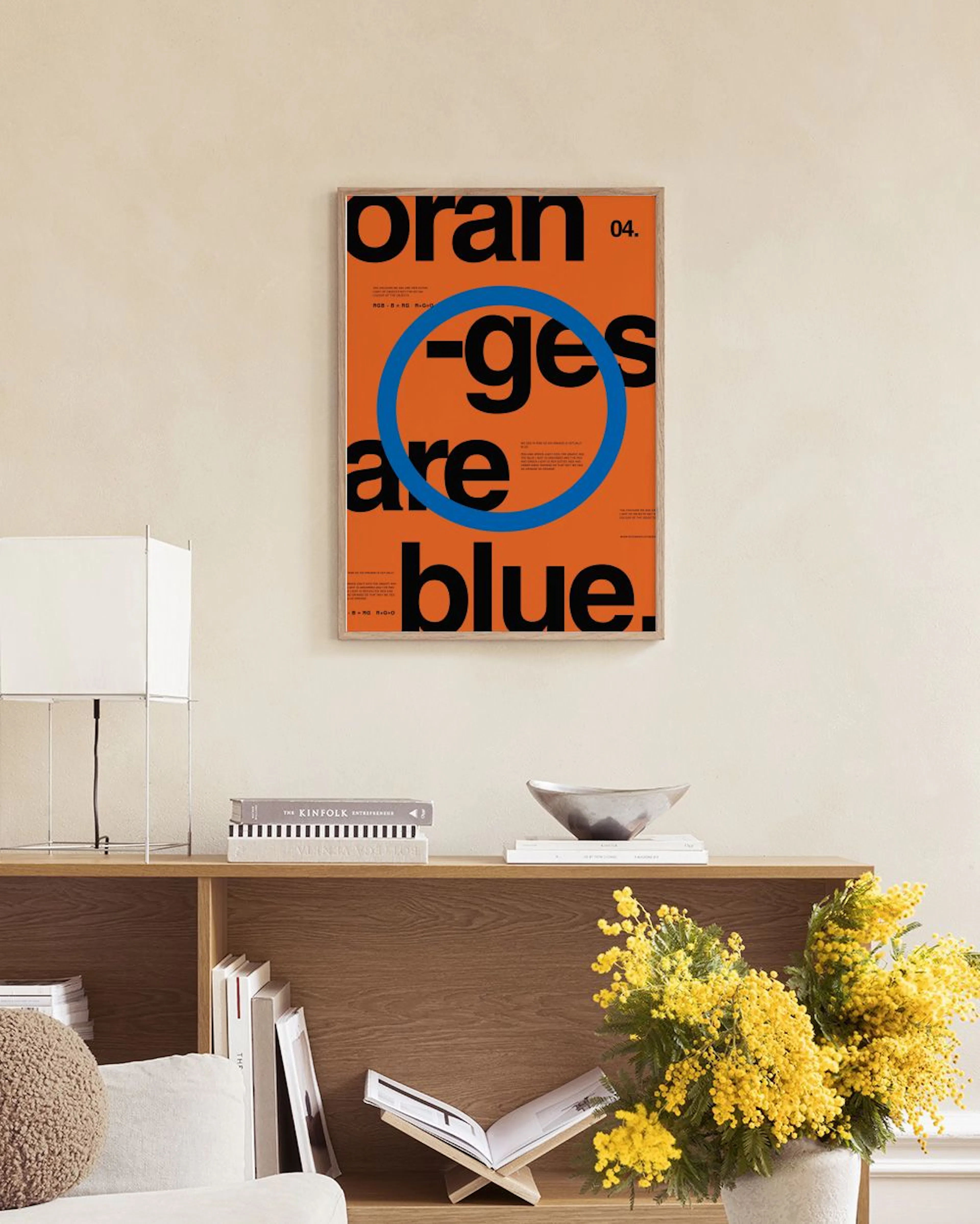 Póster oranges are blue laranja com letras pretas e anel azul, pendurado acima de um banco de verga com livros.