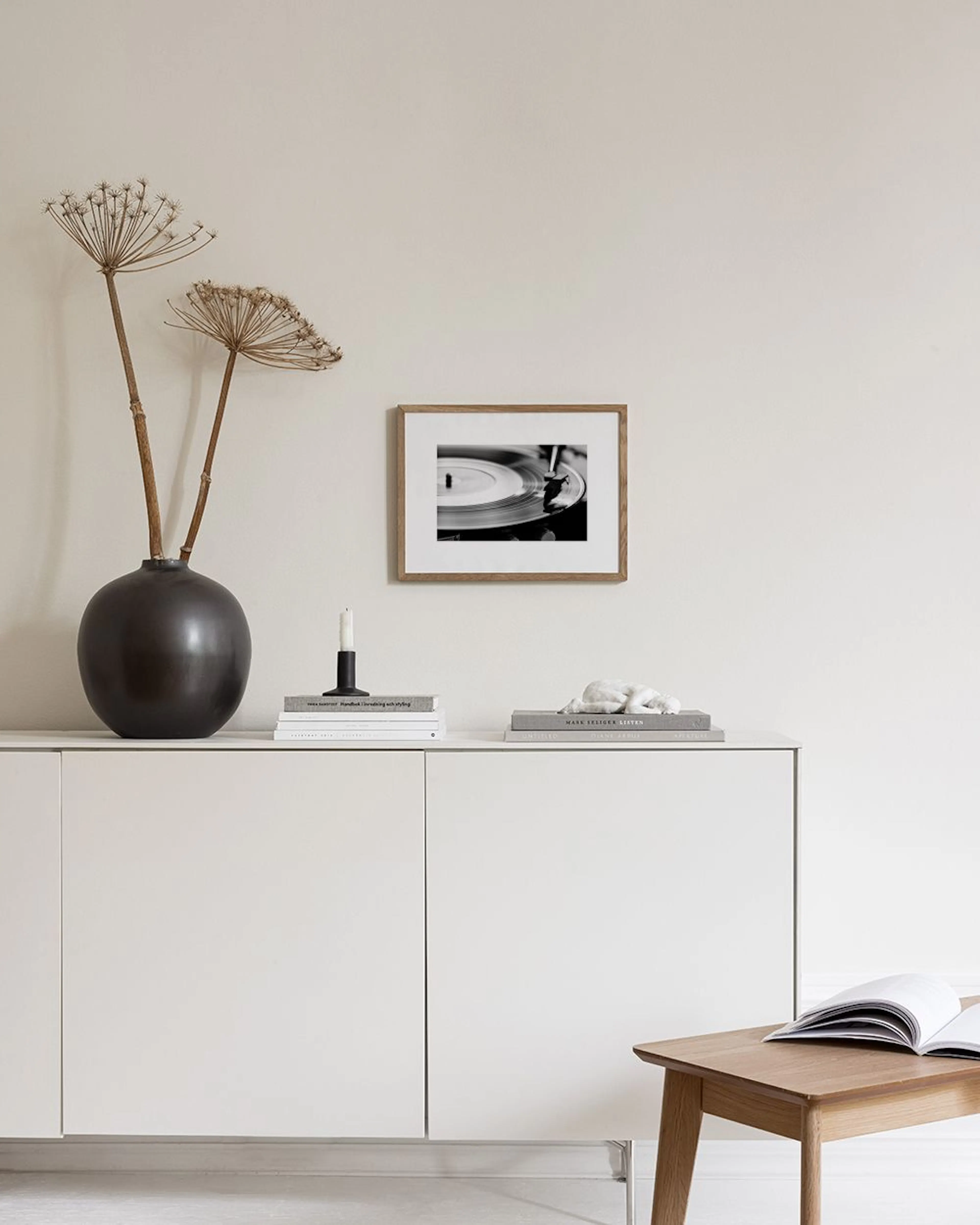 Svartvit poster av en snurrande vinylskiva på en skivspelare, hängande ovanför ett svart avlastningsbord med inredningsdetaljer.