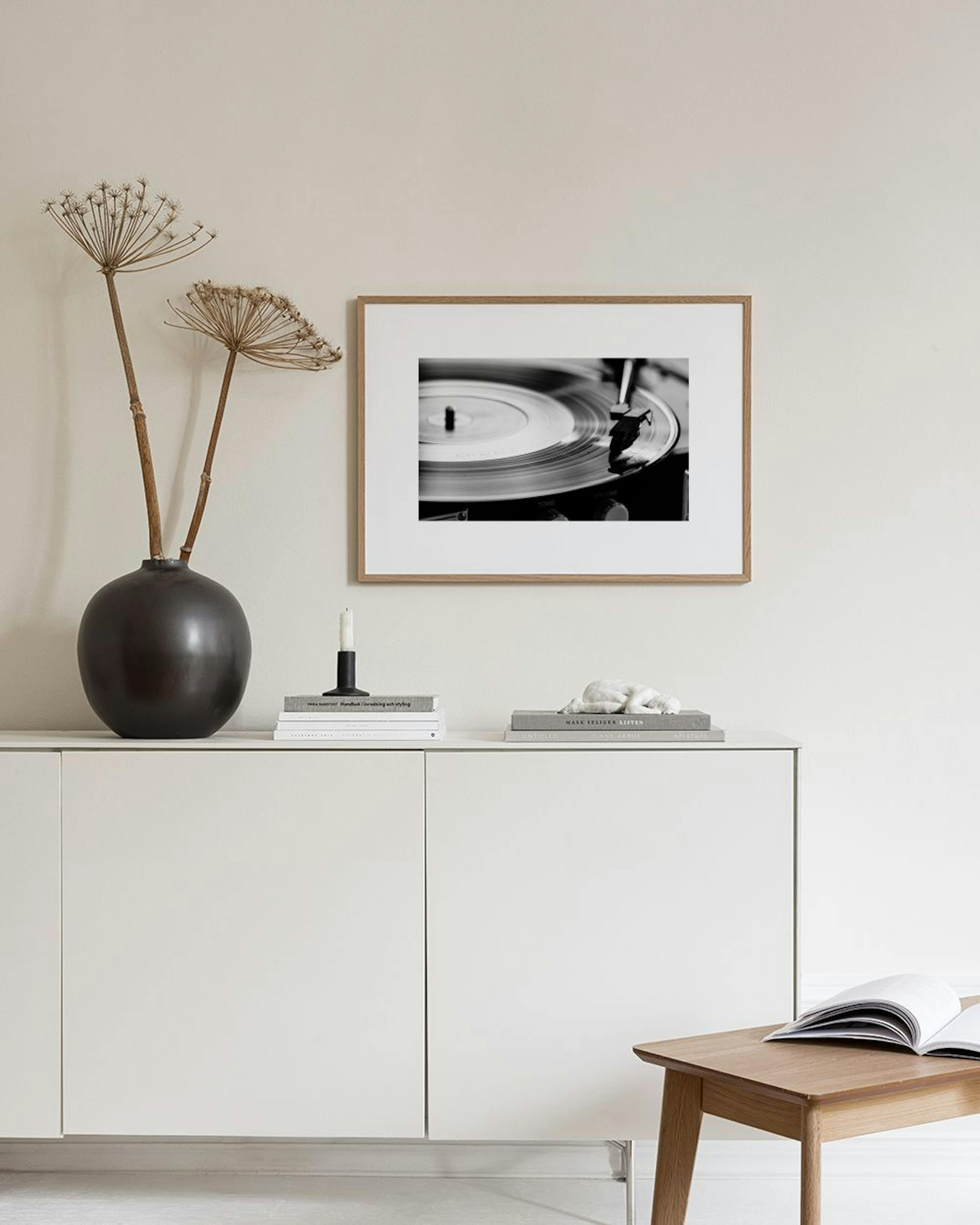 Póster a preto e branco de um gira-discos, exposto sobre uma consola preta com uma planta e objetos decorativos.
