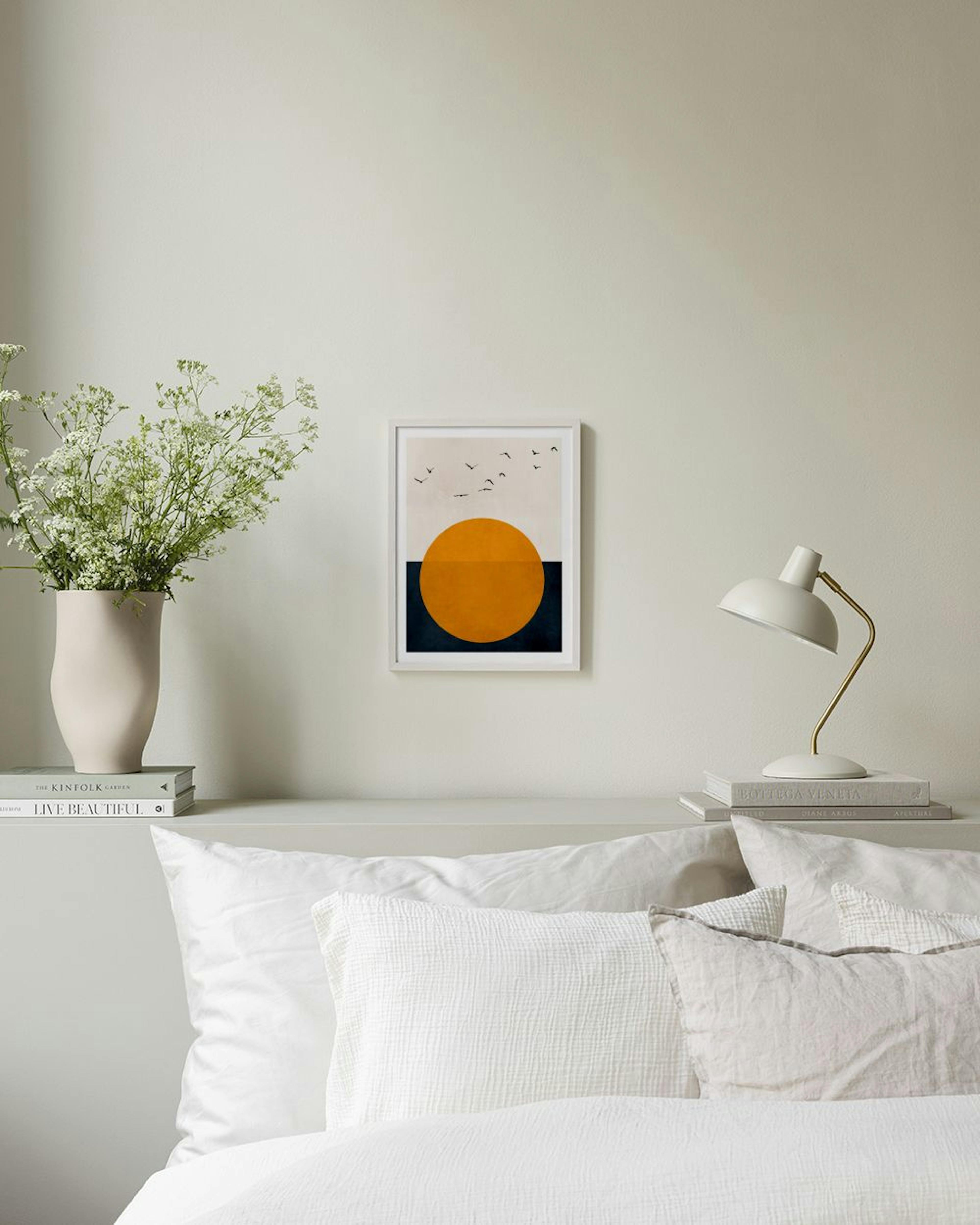 Póster abstrato com sol laranja e pássaros voadores, pendurado numa parede cinzenta, ladeado por uma cadeira e mesa laterais.