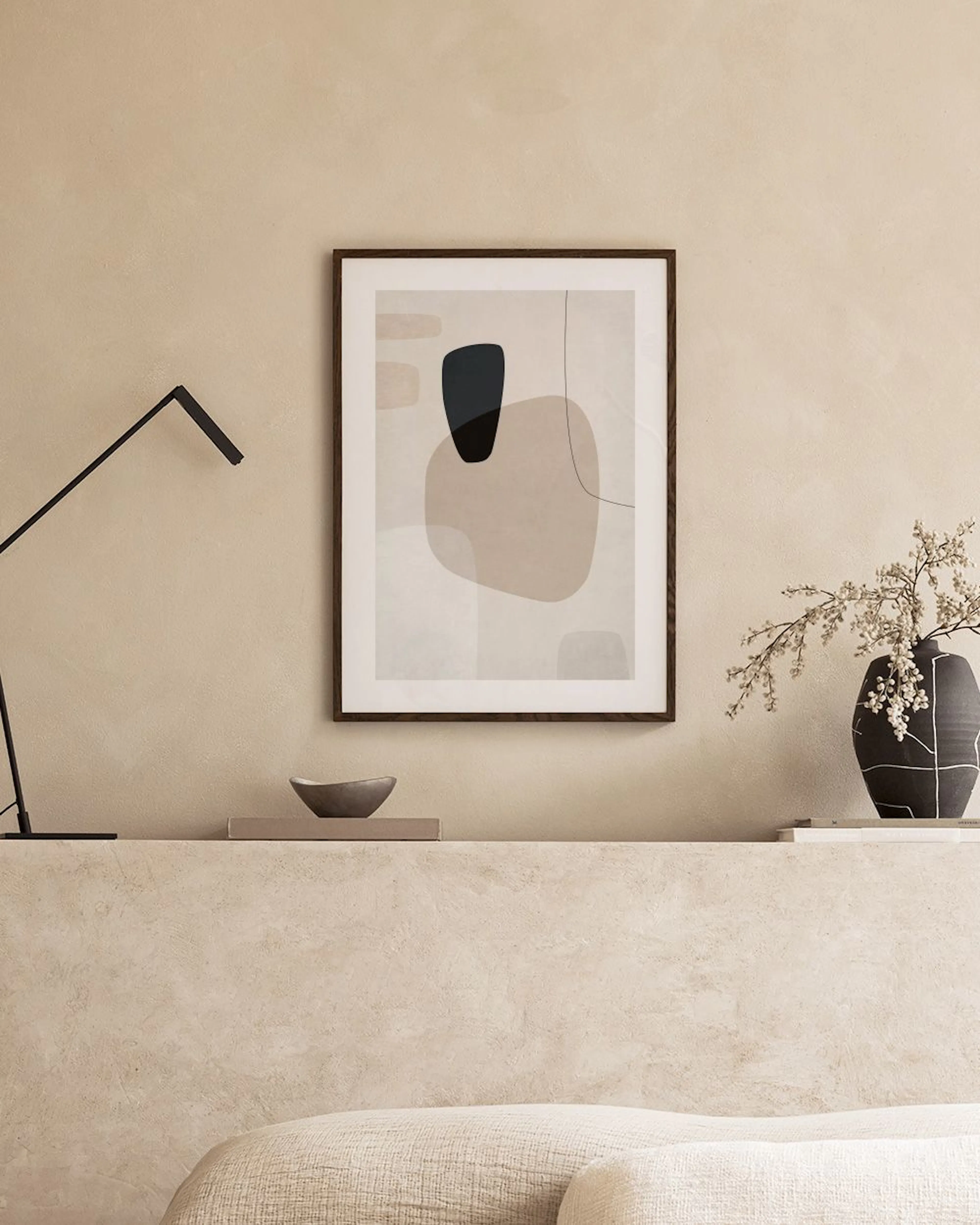 Póster abstracto con formas orgánicas en tonos beige y azul marino, junto a una mesa auxiliar y un jarrón con pampas.