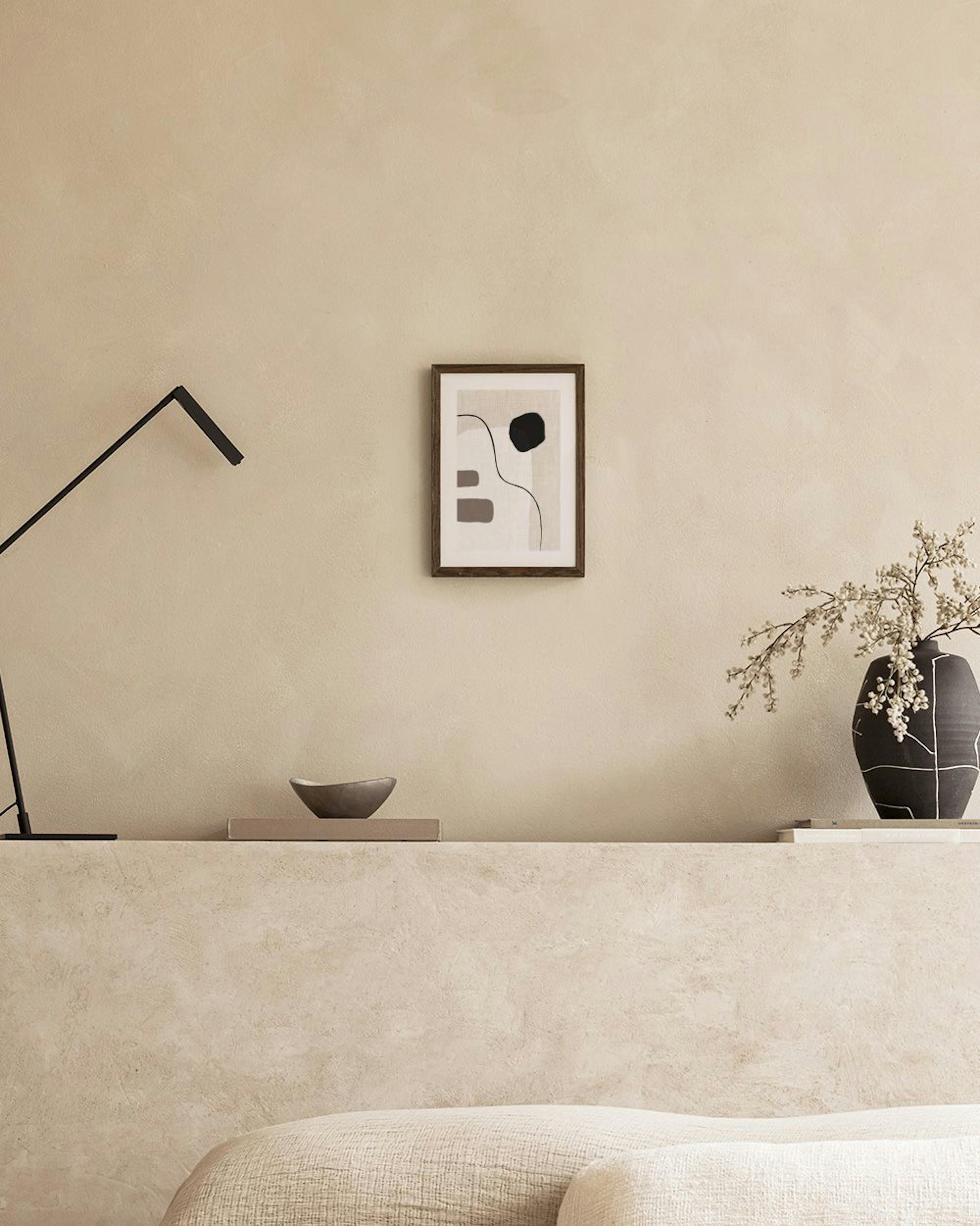 Poster con forme organiche nere, beige e marroni su sfondo chiaro, appoggiato su una panca di cemento.