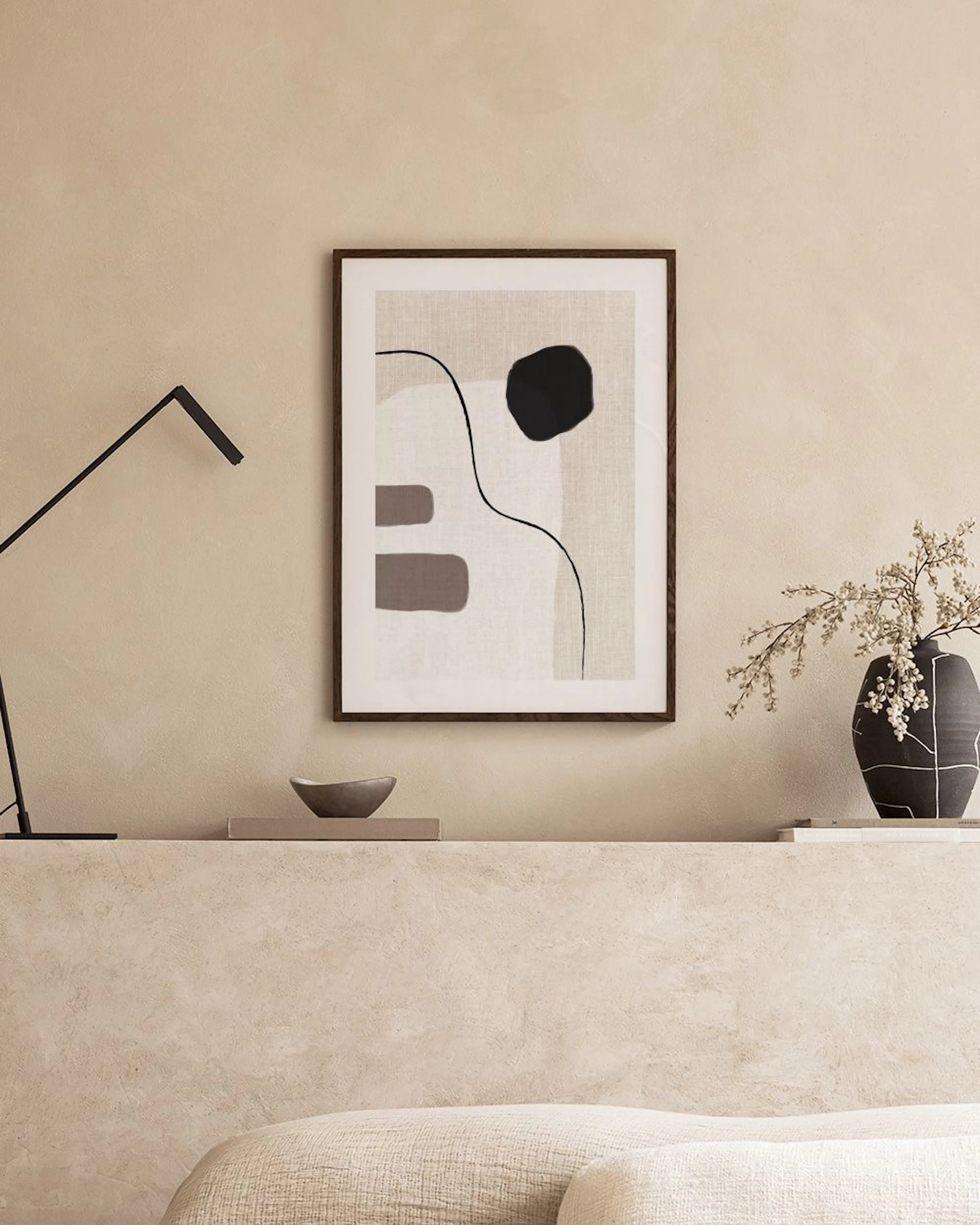 A neutral-toned abstract print with black, beige, and grey shapes, and a flowing black line, displayed on a concrete bench in a 