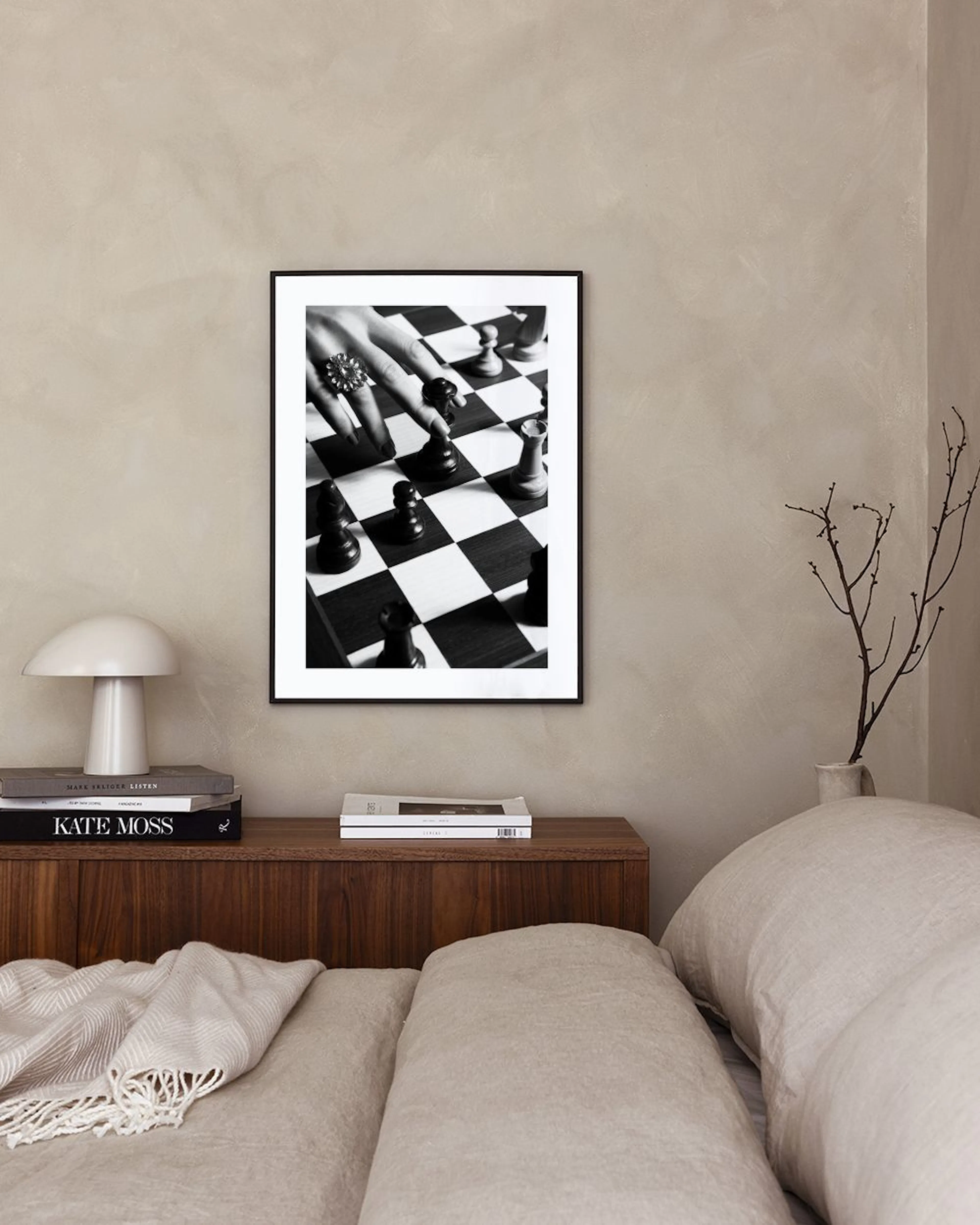 Černobílý plakát s rukou s prstenem pohybující figurkou na šachovnici, umístěný na betonovém stole s lampou.