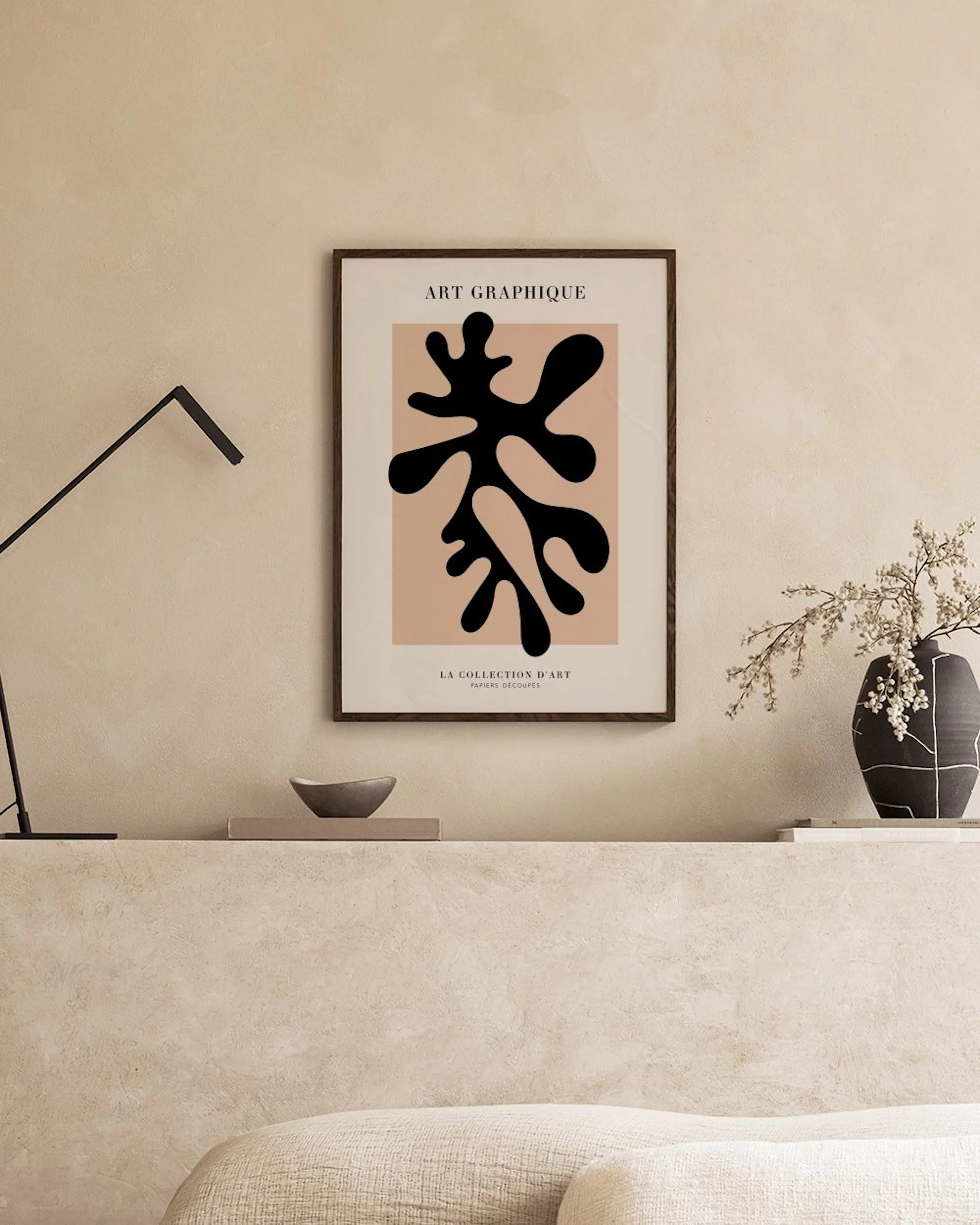 A poster with a black organic shape on a beige background, displayed on a grey console table with decorative objects and a white