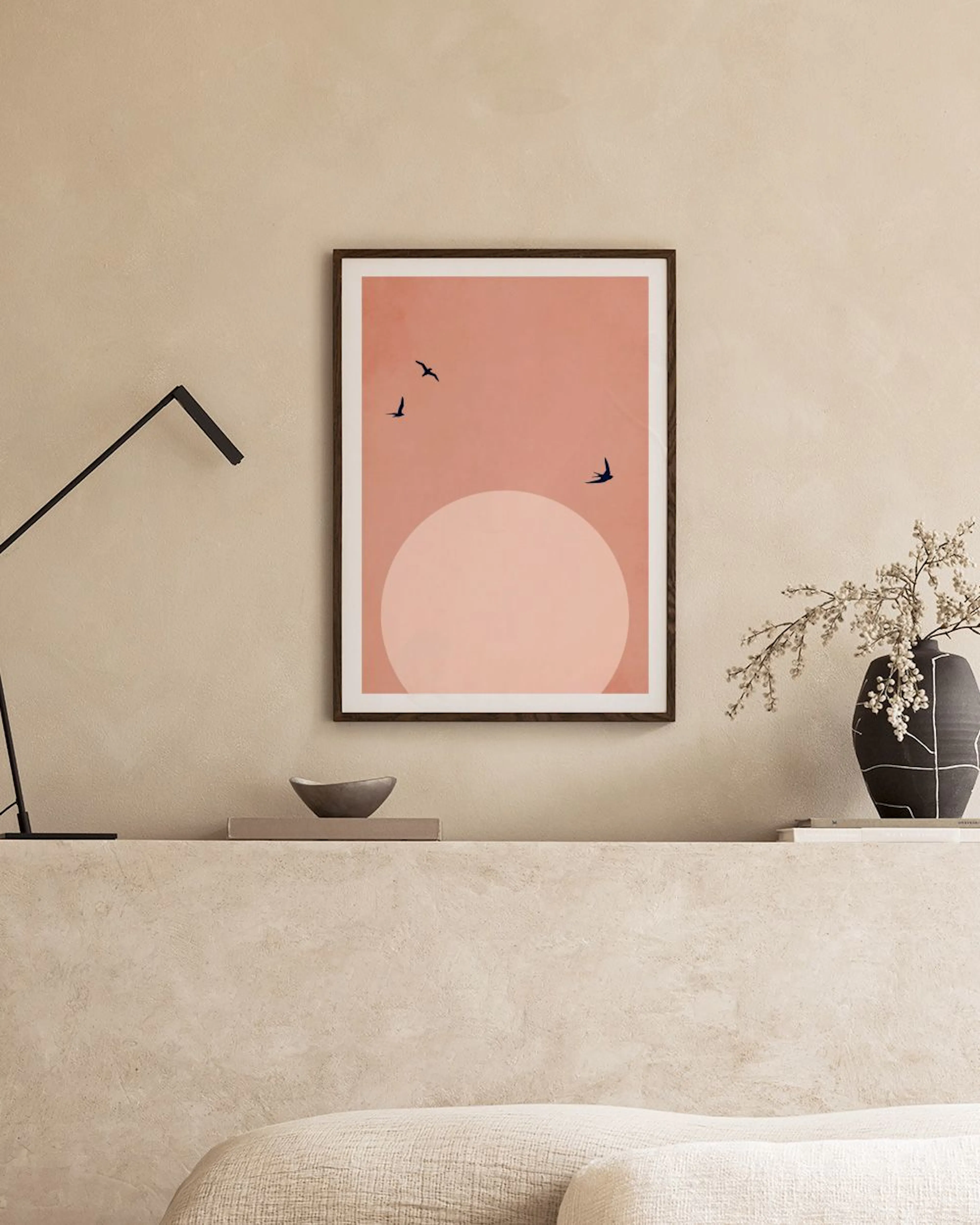 Plakat med rosa bakgrunn, lyserosa sirkel, og svarte fugler, henger over et marmorbord med vaser og bøker.