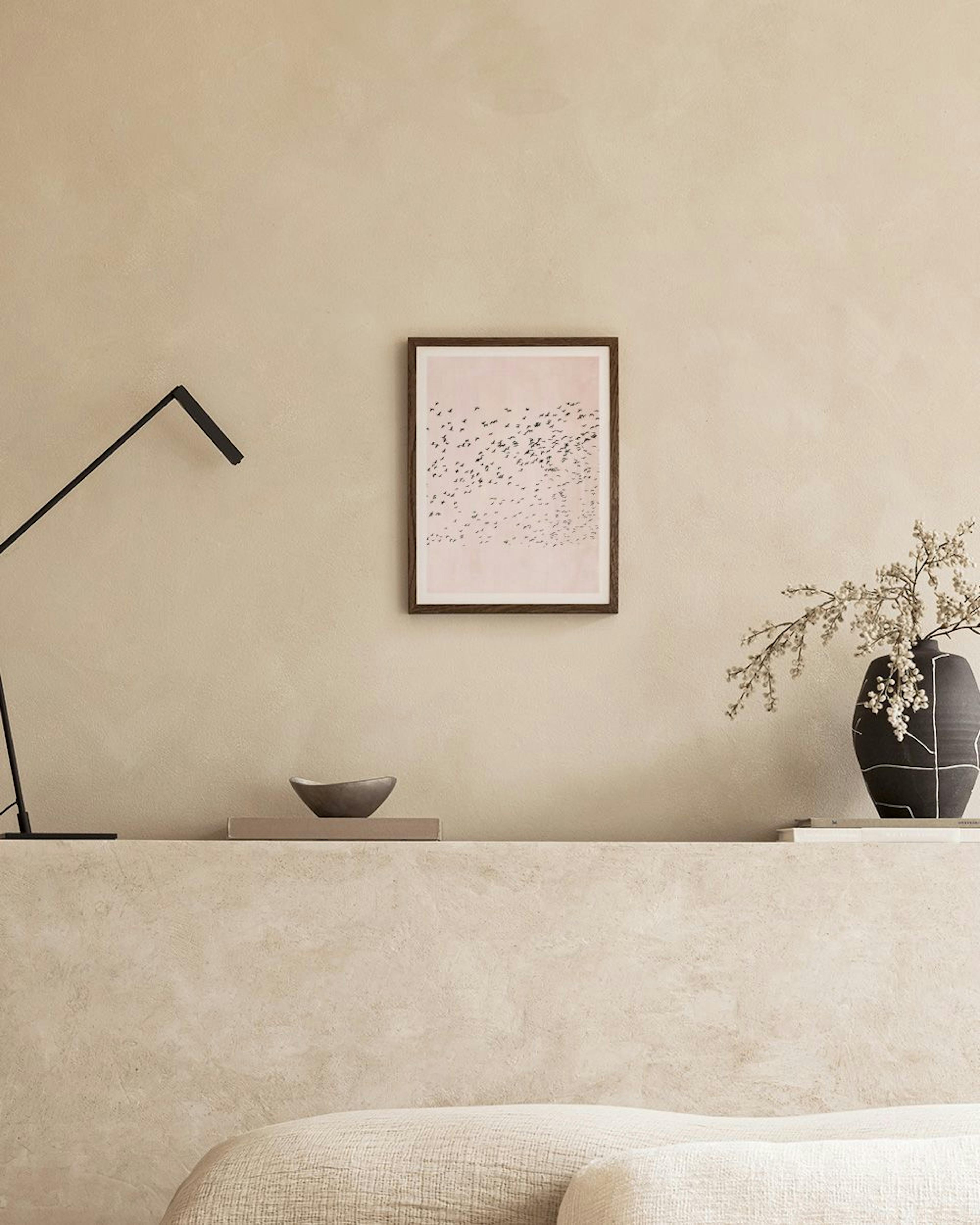 Affiche avec un vol doiseaux noirs sur fond rose pâle, accrochée au mur dune pièce moderne avec un tabouret et une vase.