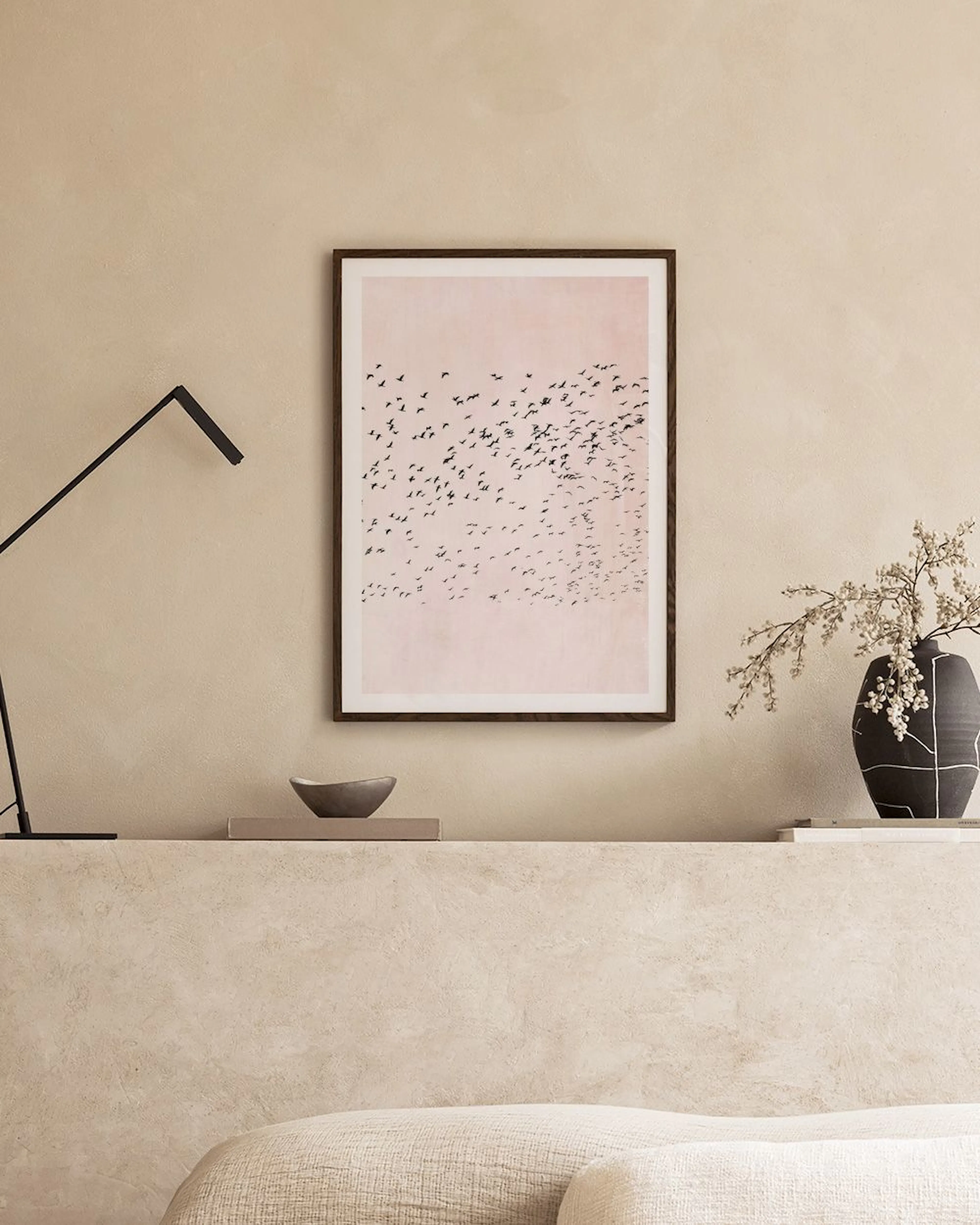 A print of a flock of black birds against a dusty pink background, hanging on a light gray wall above a white cabinet.