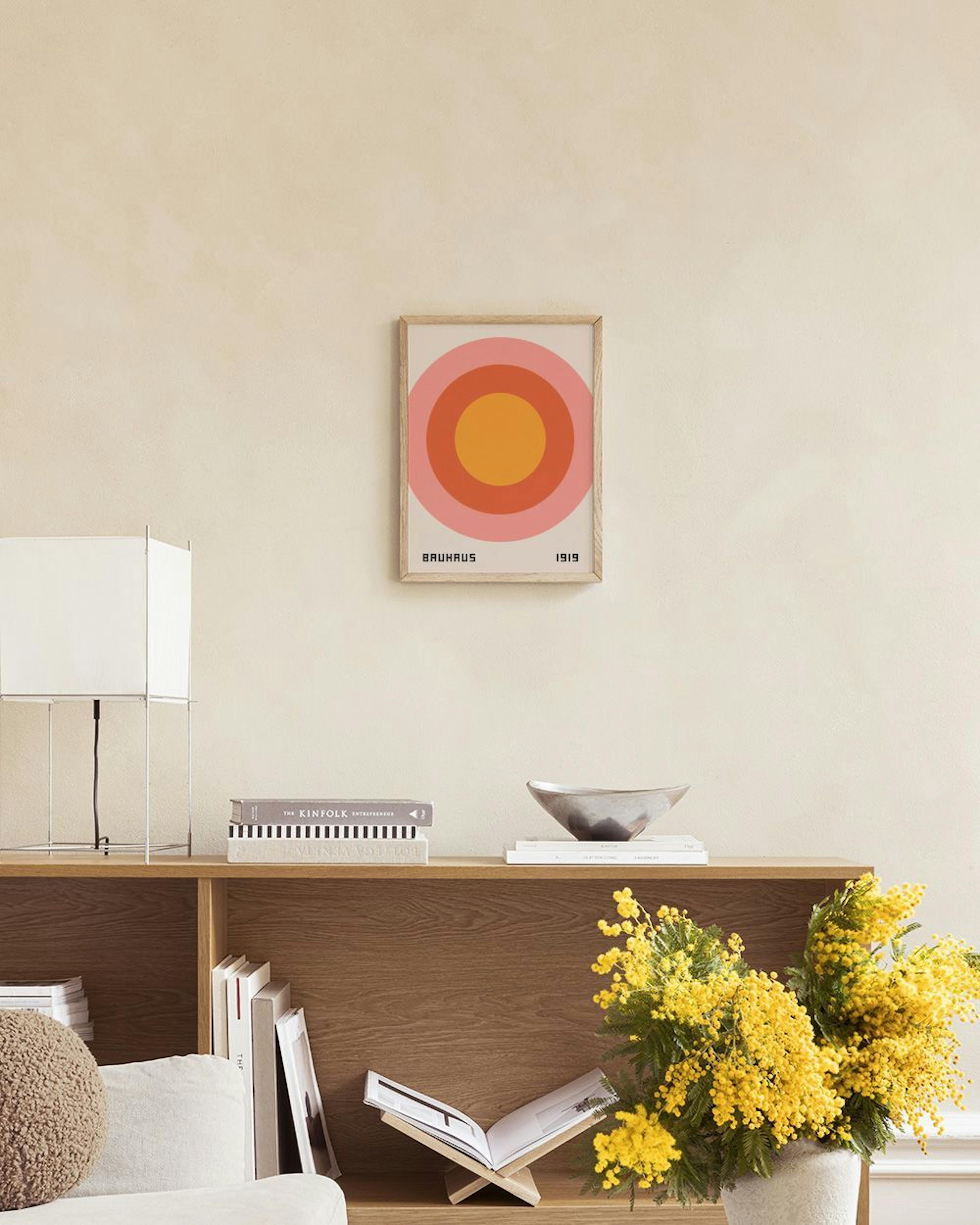 Affiche Bauhaus avec cercles concentriques roses, orange et terracotta, affichée au-dessus dun buffet en rotin.