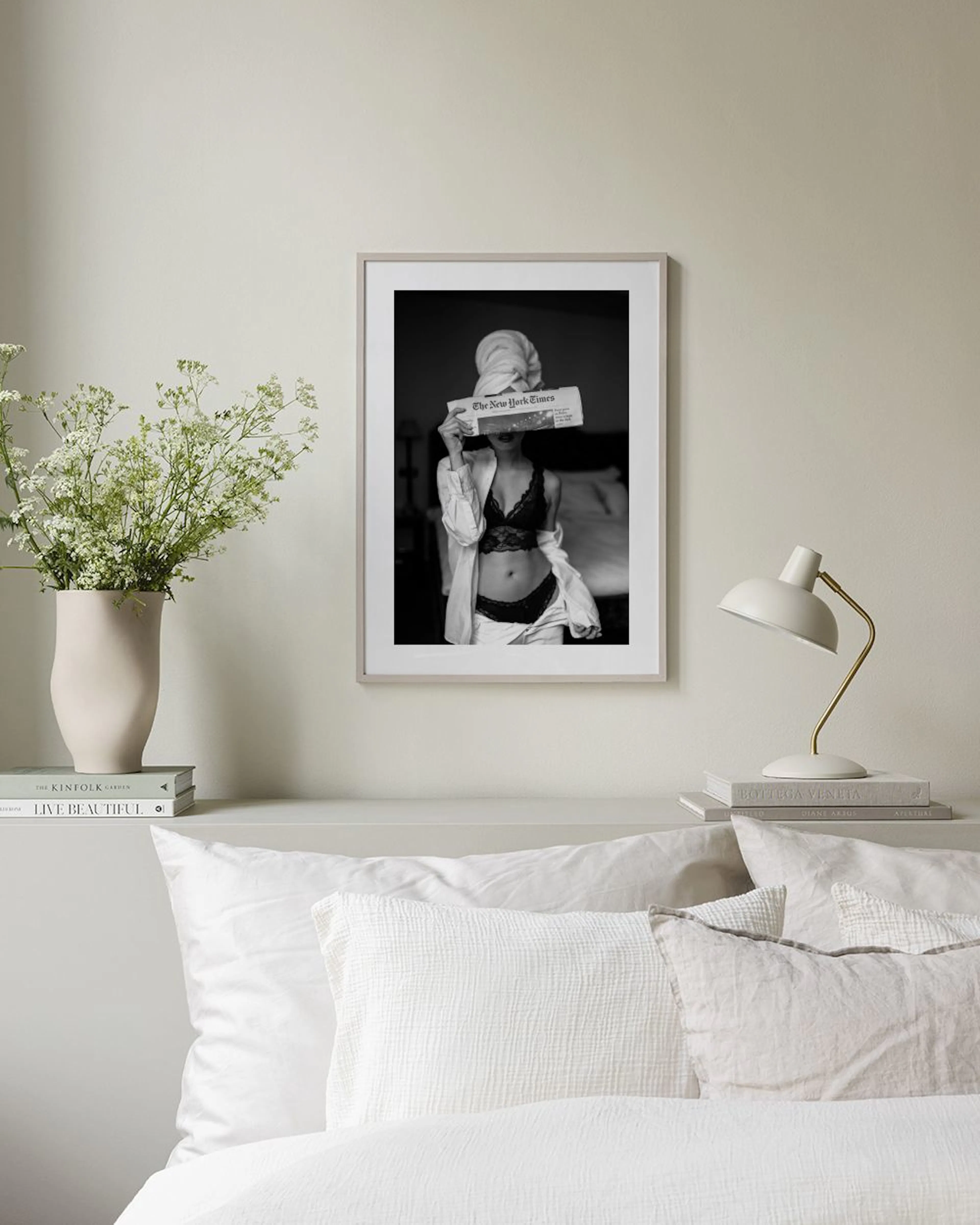 A black and white print of a woman in lingerie and a towel on her head, holding a newspaper, displayed above a brown sofa in a l