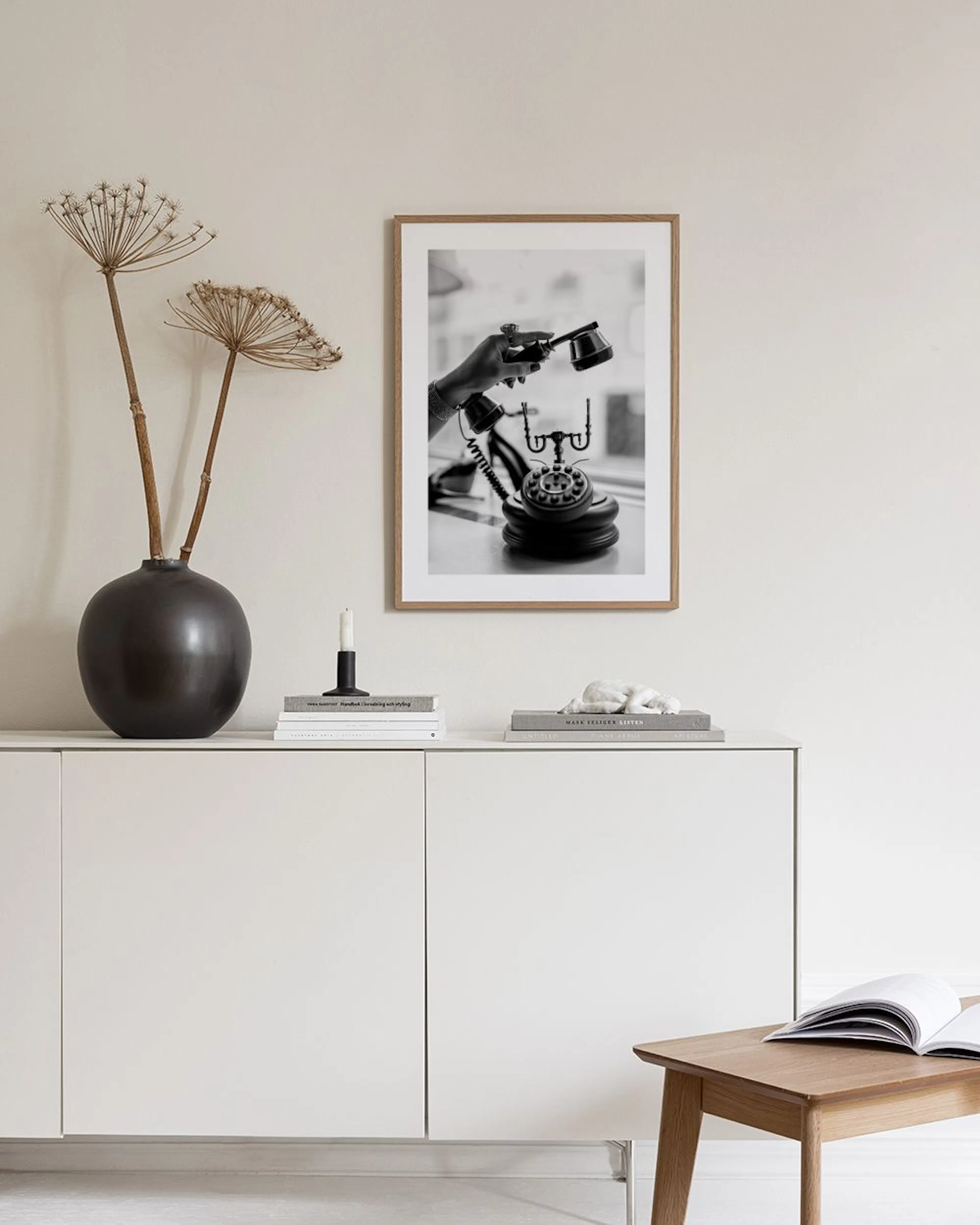 A black and white print of a hand holding a vintage telephone receiver, displayed on a grey cabinet with books and decor.