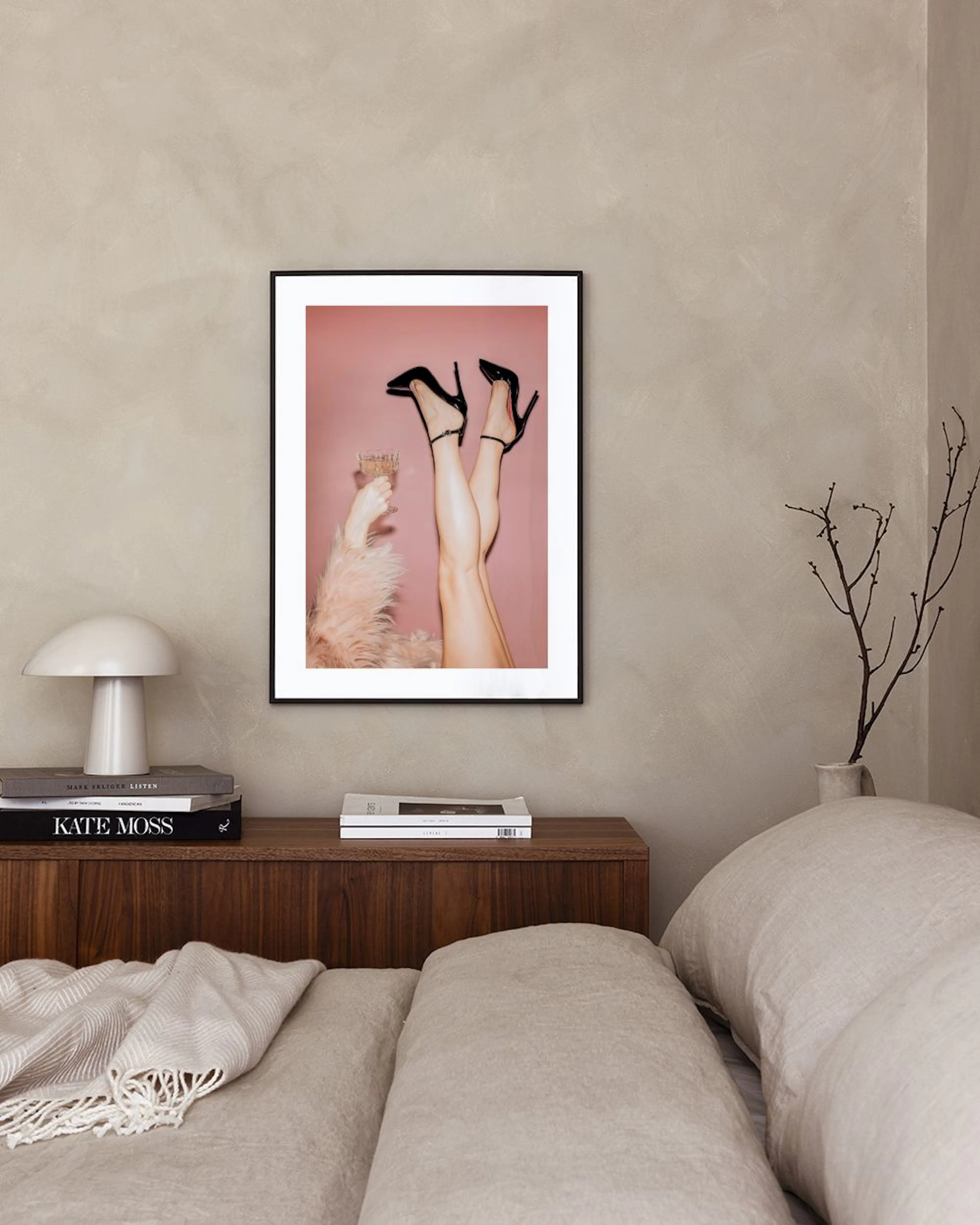 Poster mit Frauenbeinen in High Heels, die ein Glas halten, hängt in einem modernen Raum über einem Beistelltisch.