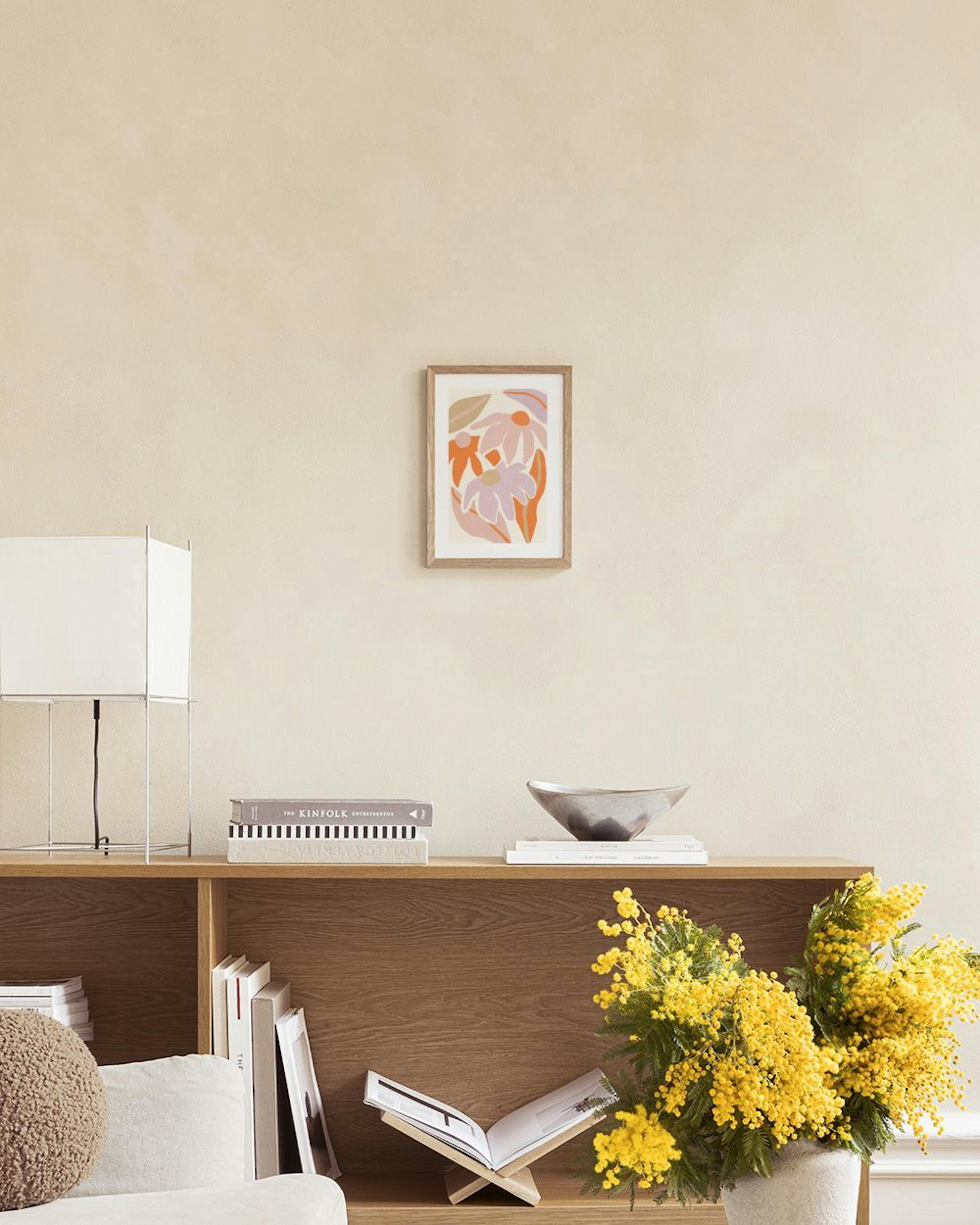 Print of abstract floral shapes in pink, orange, and beige, hanging on a white wall above a purple ottoman.