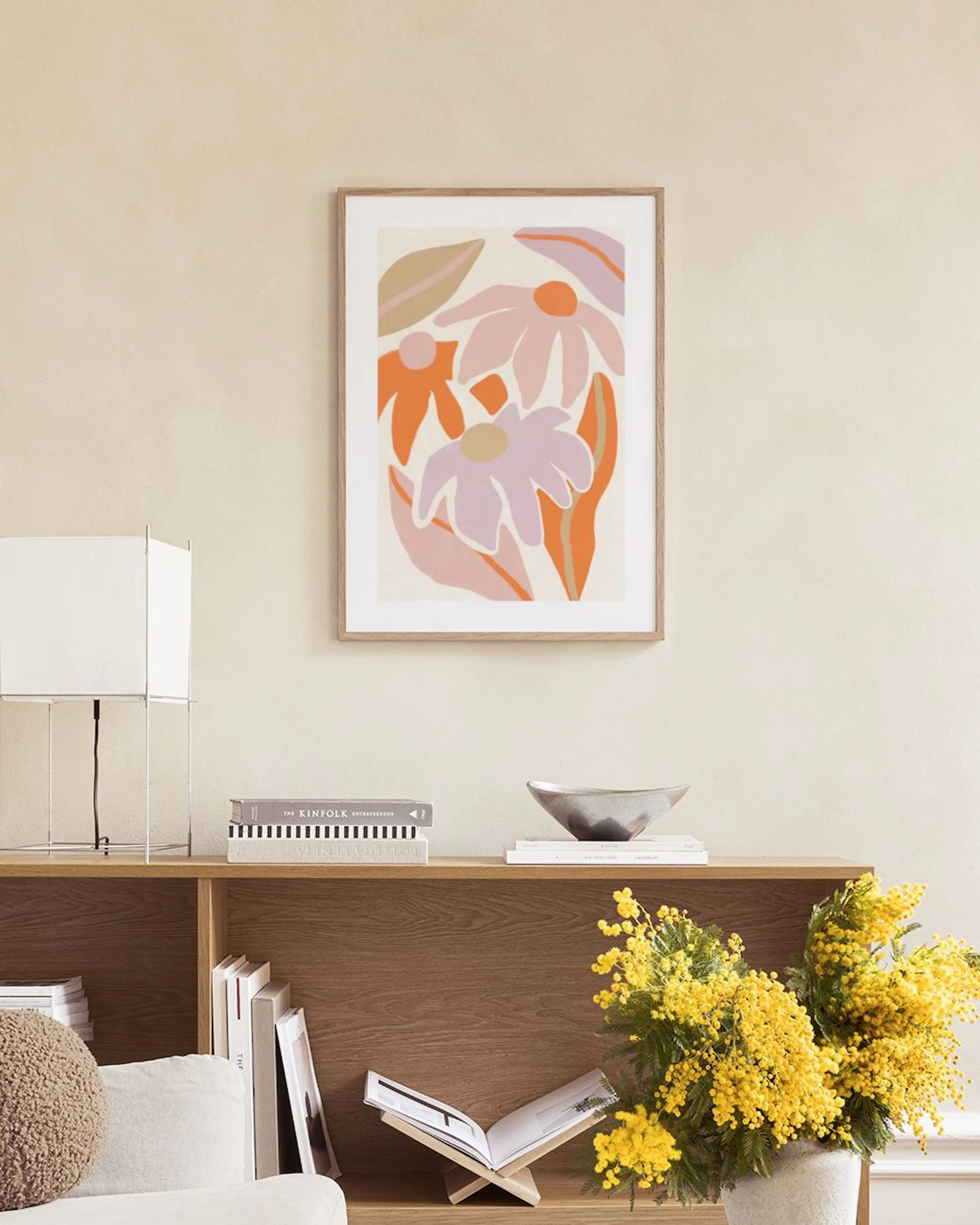 Affiche murale de fleurs abstraites roses et orangées, suspendue au-dessus dun pouf lilas et à côté dun socle blanc.
