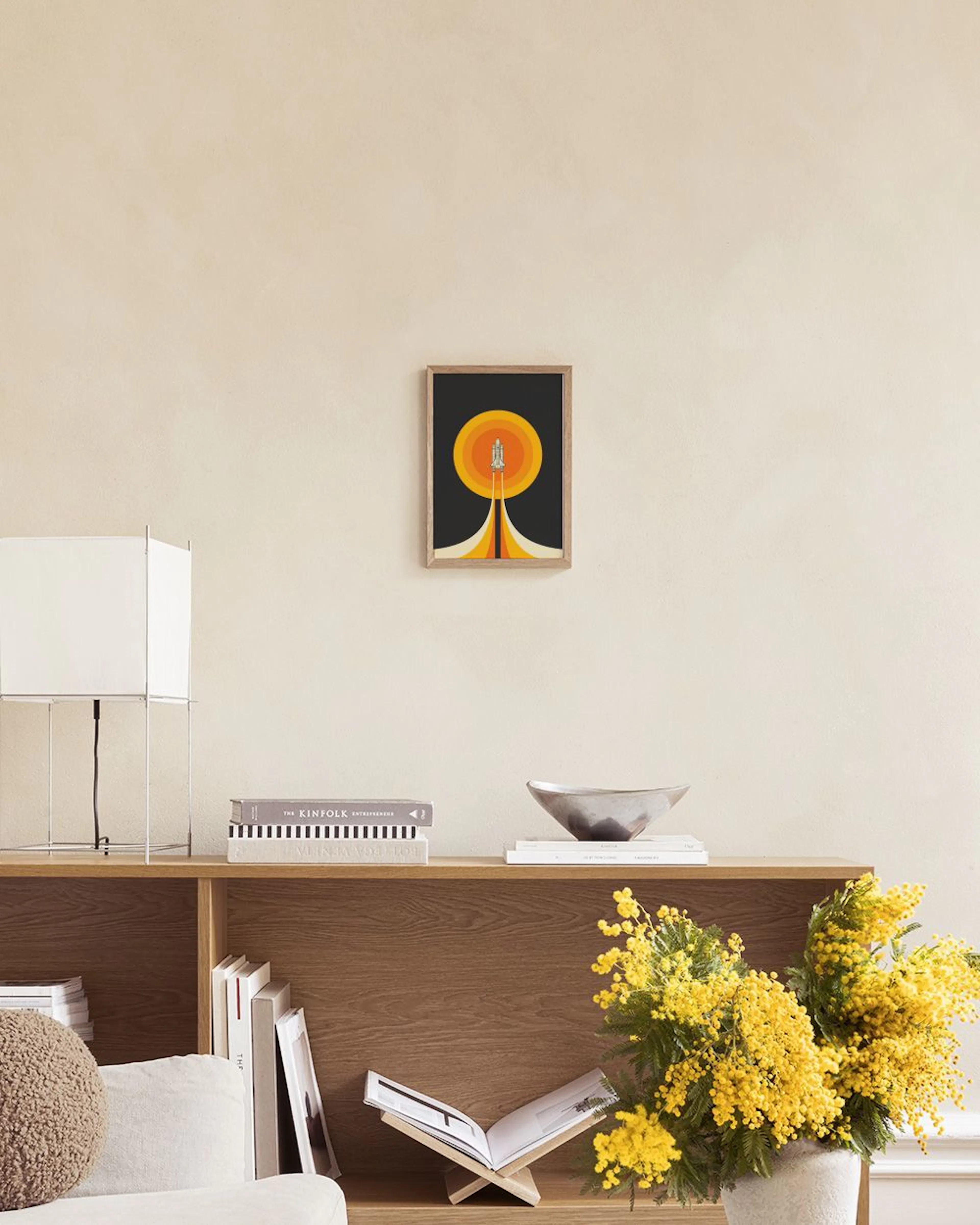 A space shuttle print with orange and yellow sun shapes, displayed on a grey console table with decorative balls and a white lam