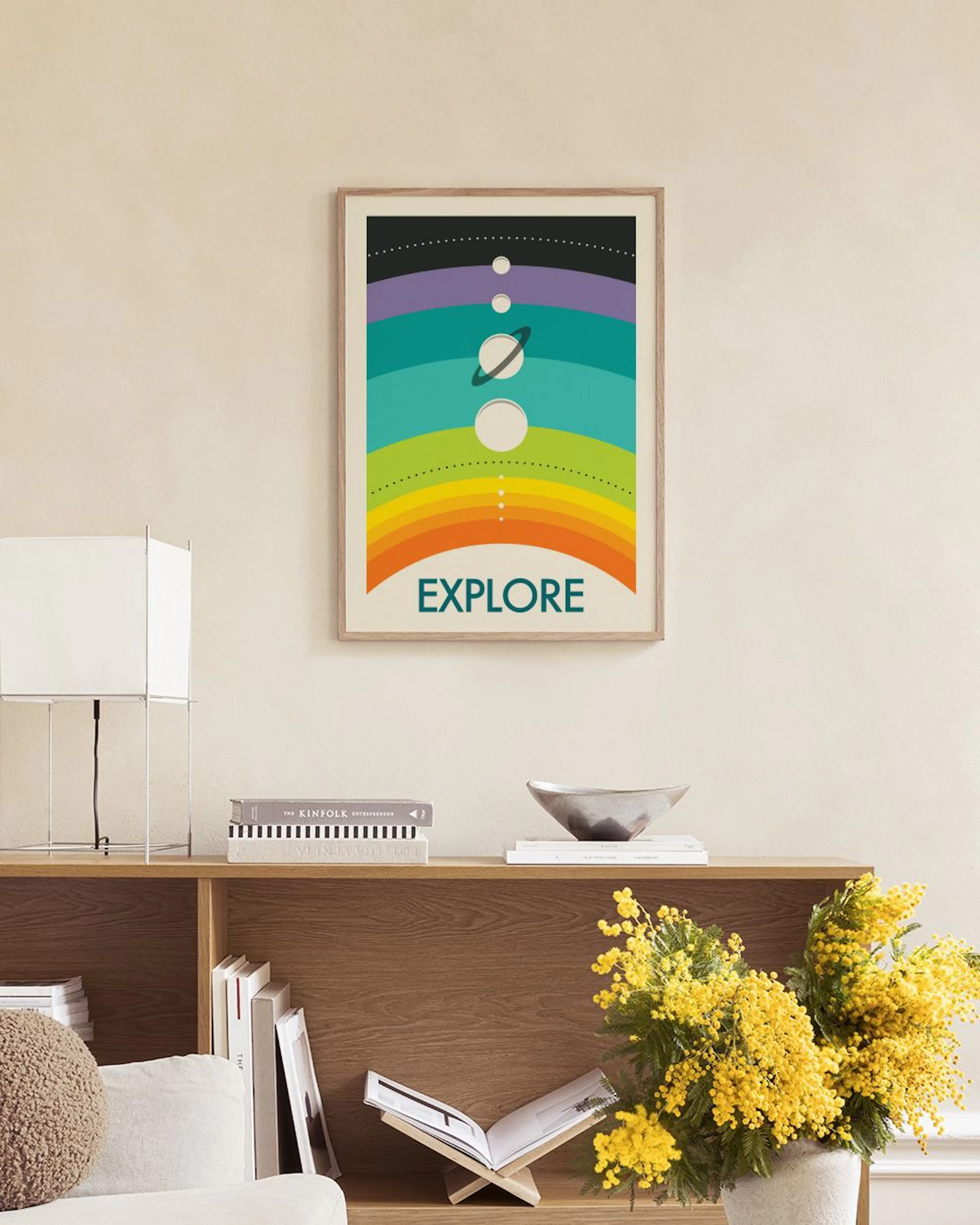Plakat Explore” z kolorowymi pasami, słońcem i planetami, wiszący nad marmurowym stolikiem z białymi wazonami.