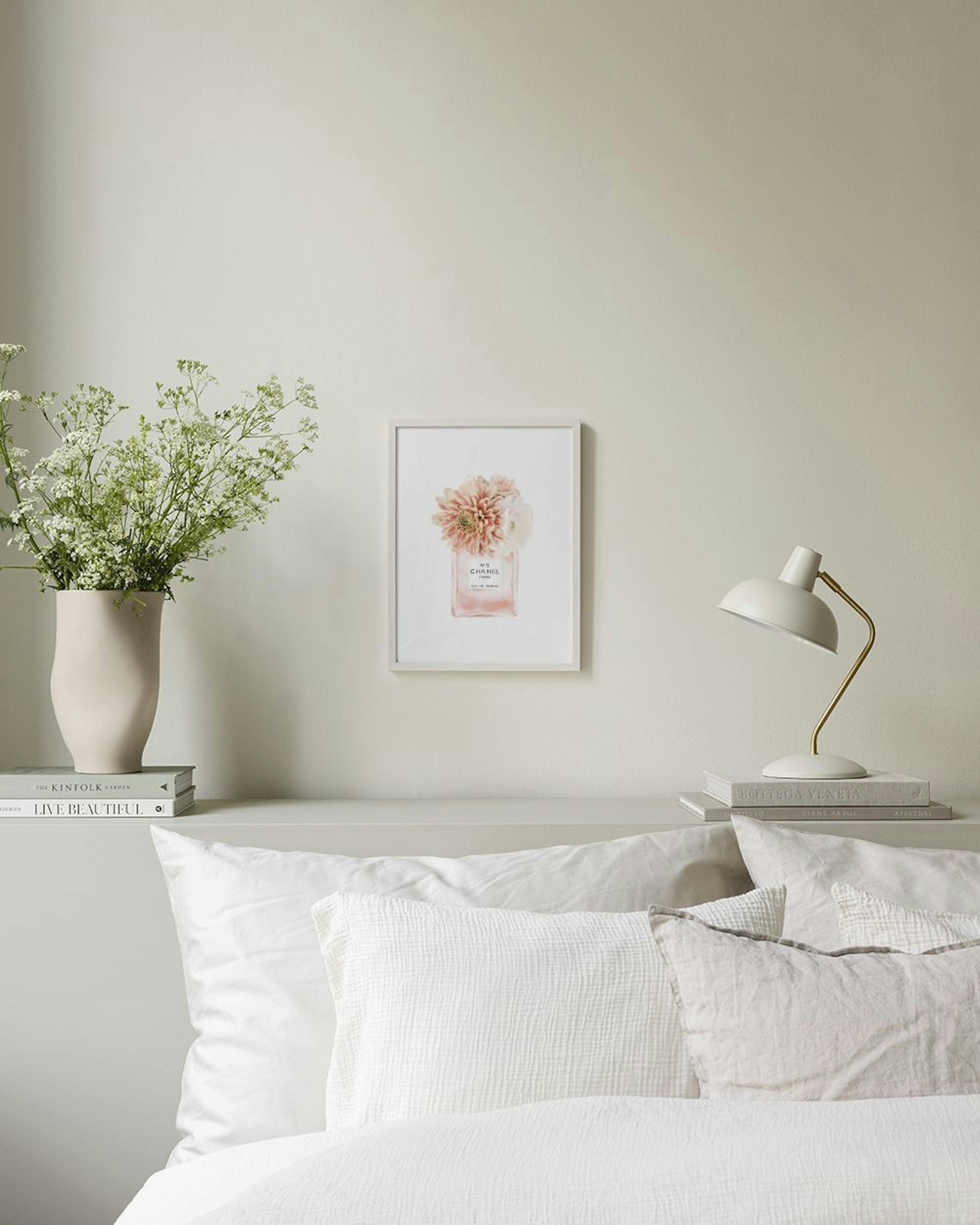 Poster van een parfumflesje met roze bloemen, hangend boven een wit dressoir met beige vazen en boeken.