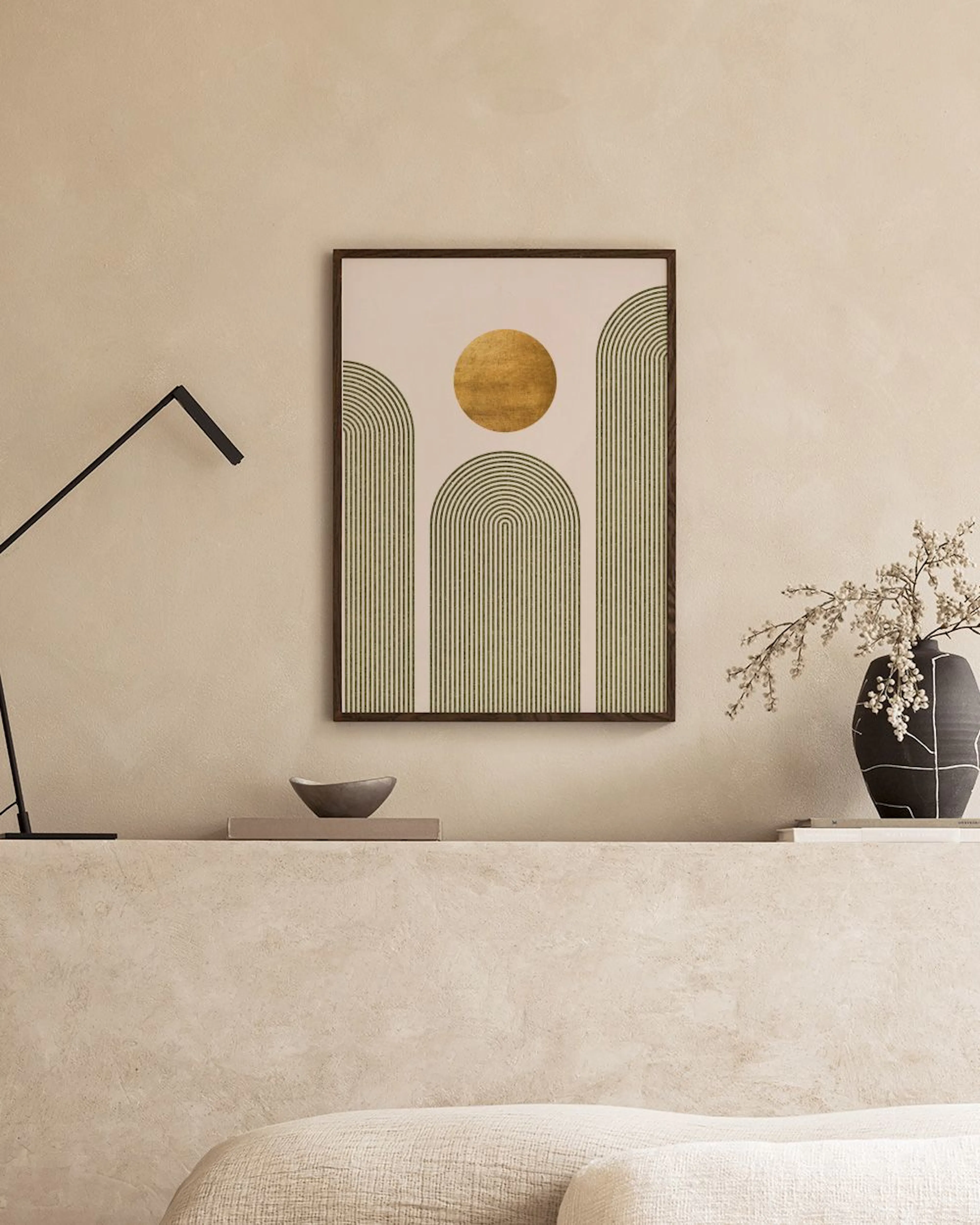 A print with a golden circle and black striped arches on a cream background, hanging above a green ottoman.