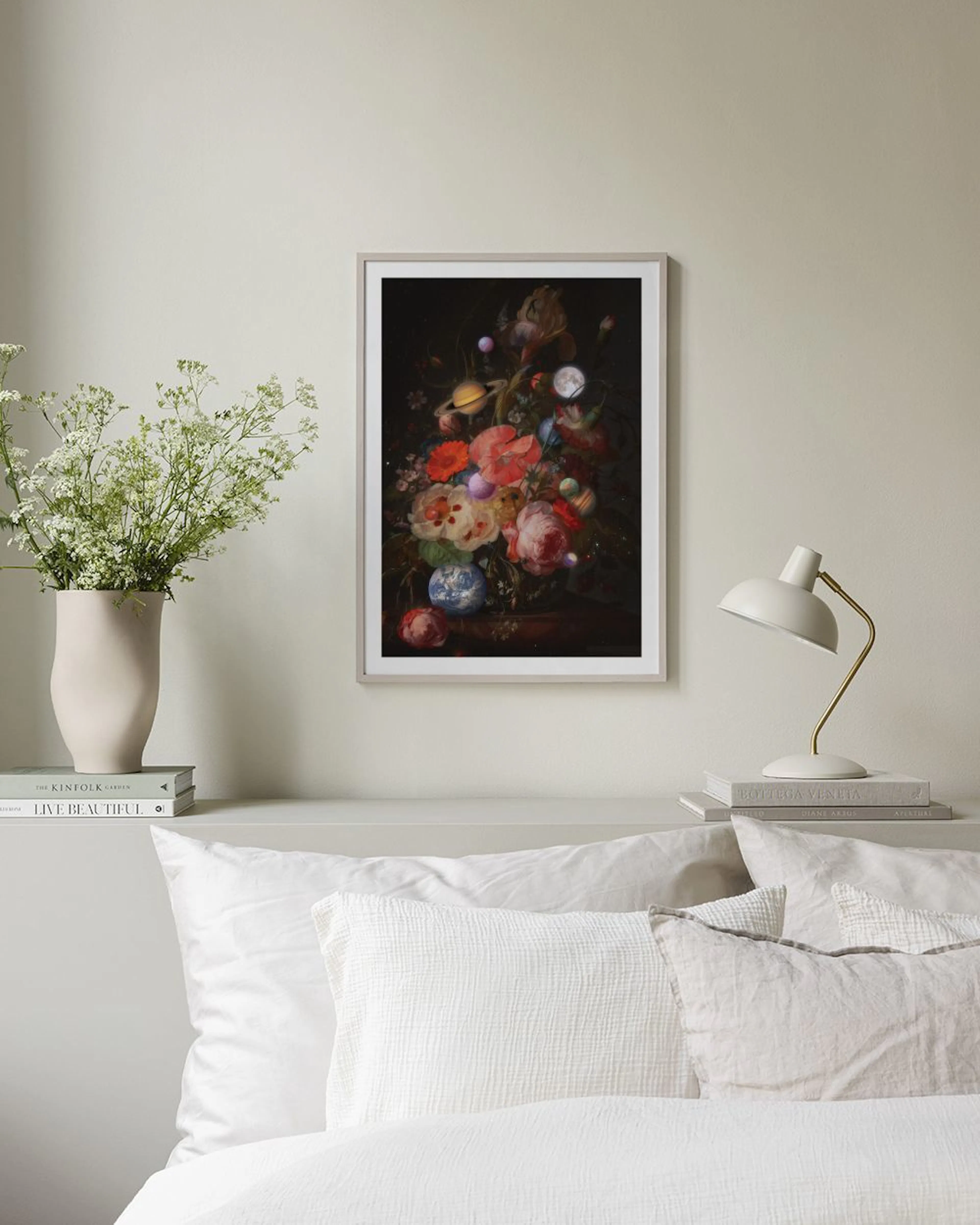 A cosmic floral print with planets and moons among vibrant flowers, hanging above a black shelf with books and decor.