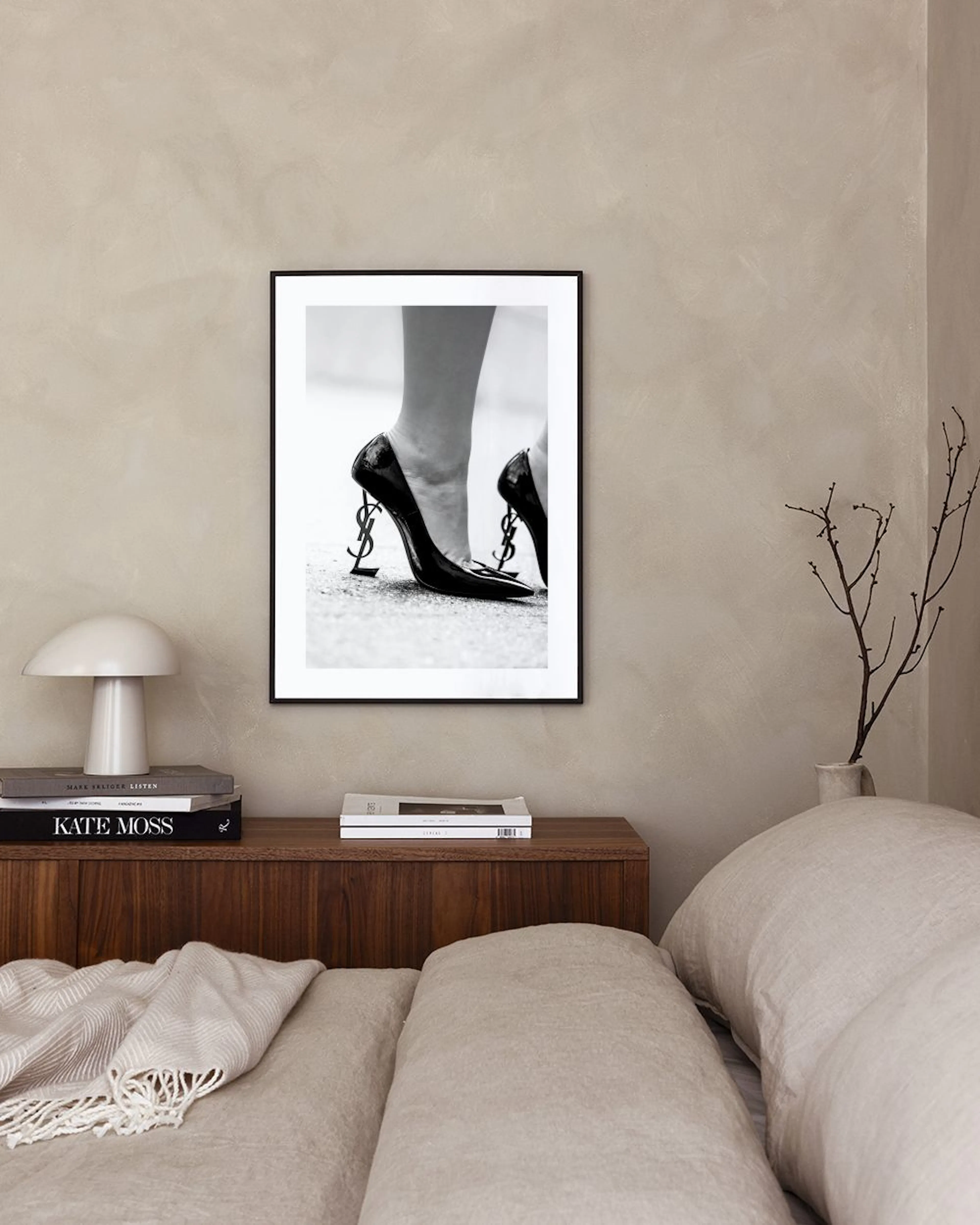 Plakat med svart-hvitt fotografi av føtter som står i svarte høyhælte sko med YSL-logoen som hæl, henger i et moderne rom over e