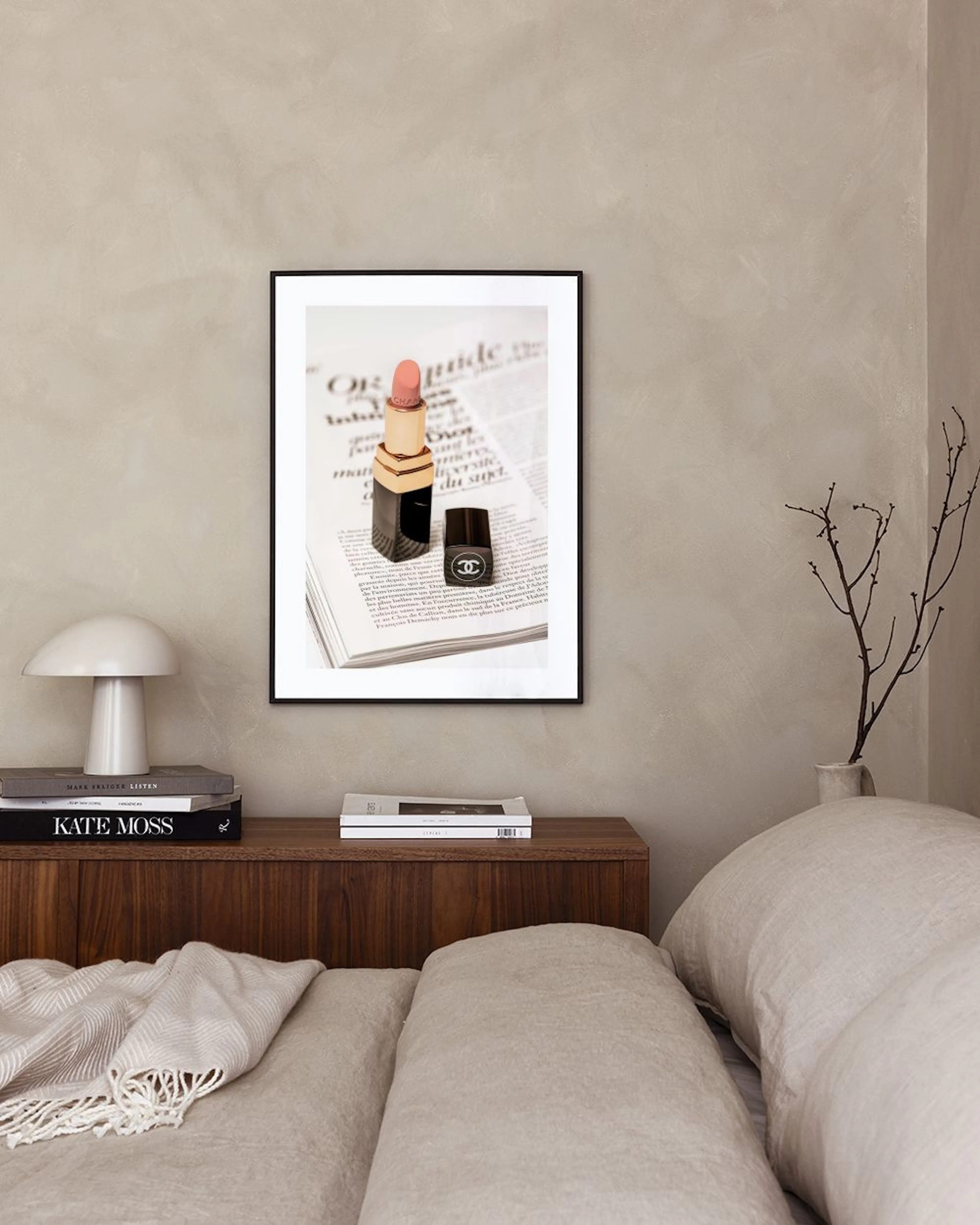 A print of a pink lipstick and Chanel nail polish on a newspaper, hanging above a pink dresser with books.