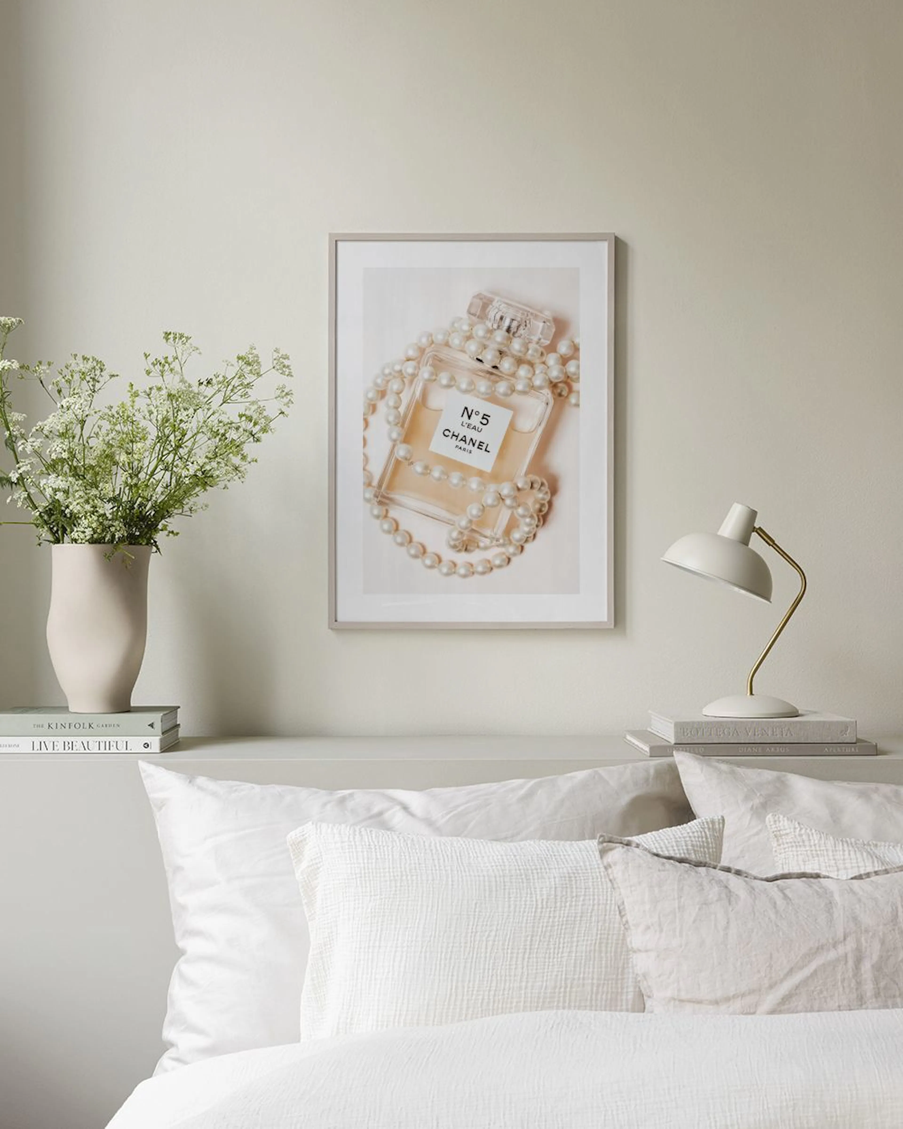Poster van een Chanel N°5 parfumfles omringd door parels, boven een houten bankje met vazen en boeken.