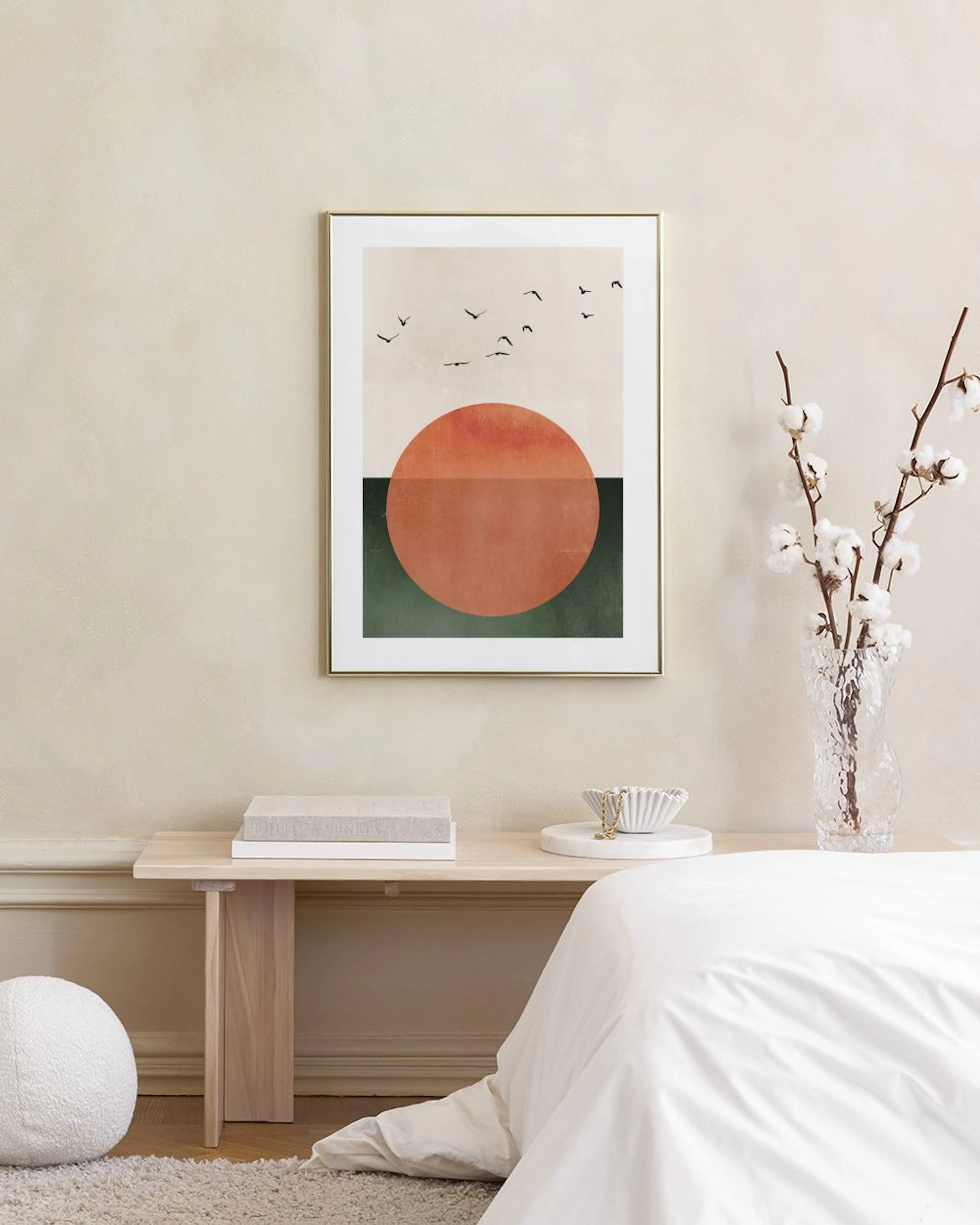 Un poster con sole arancione, terra verde e uccelli in volo, appeso sopra una credenza grigio-verde con libri e un vassoio decor