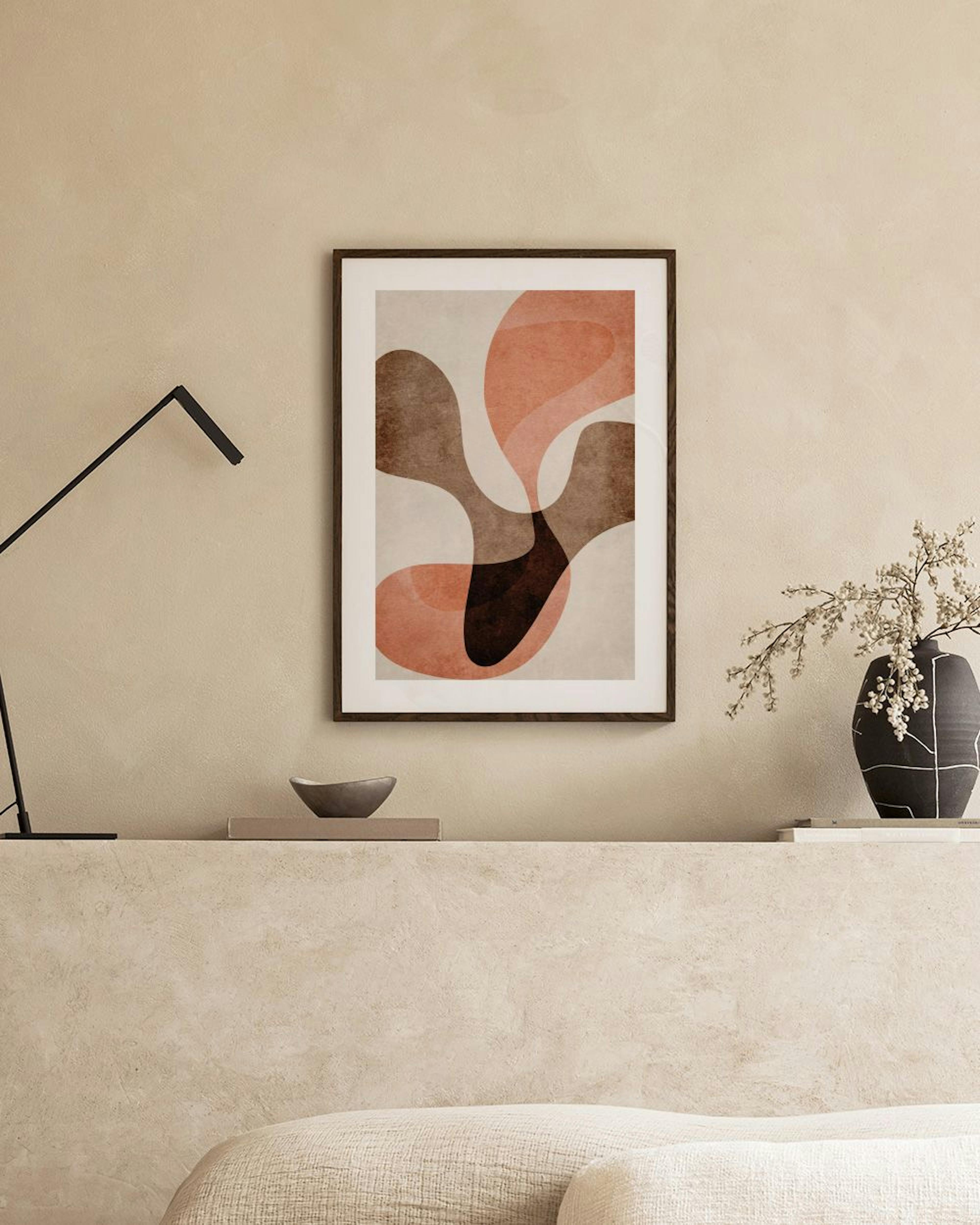 Poster med abstrakta former i brunt, beige och laxrosa toner, hängande ovanför ett vitt skåp med vaser och böcker.
