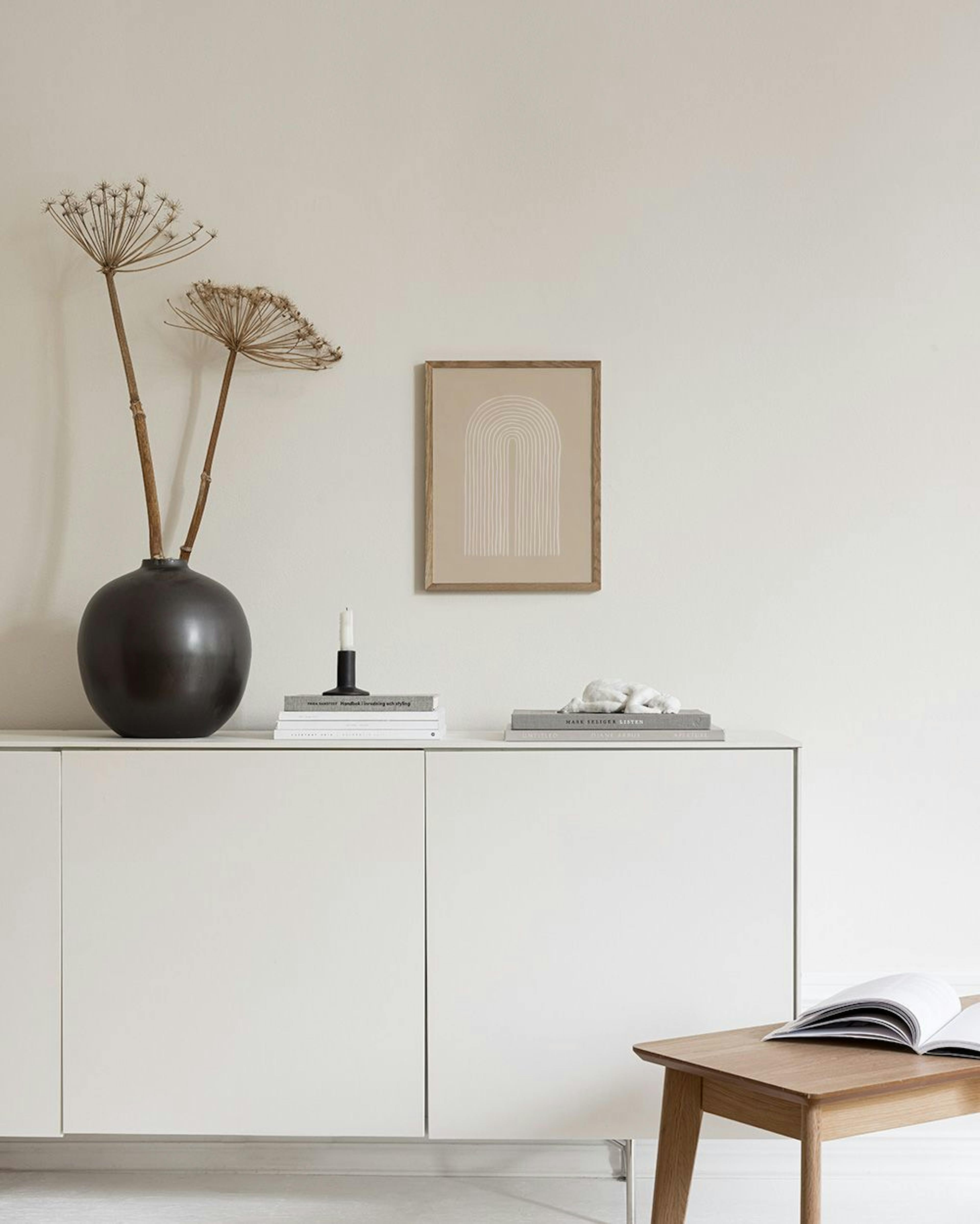 Poster met abstracte witte lijnen die een boog vormen op een beige achtergrond, hangend boven een marmeren bijzettafel met vazen