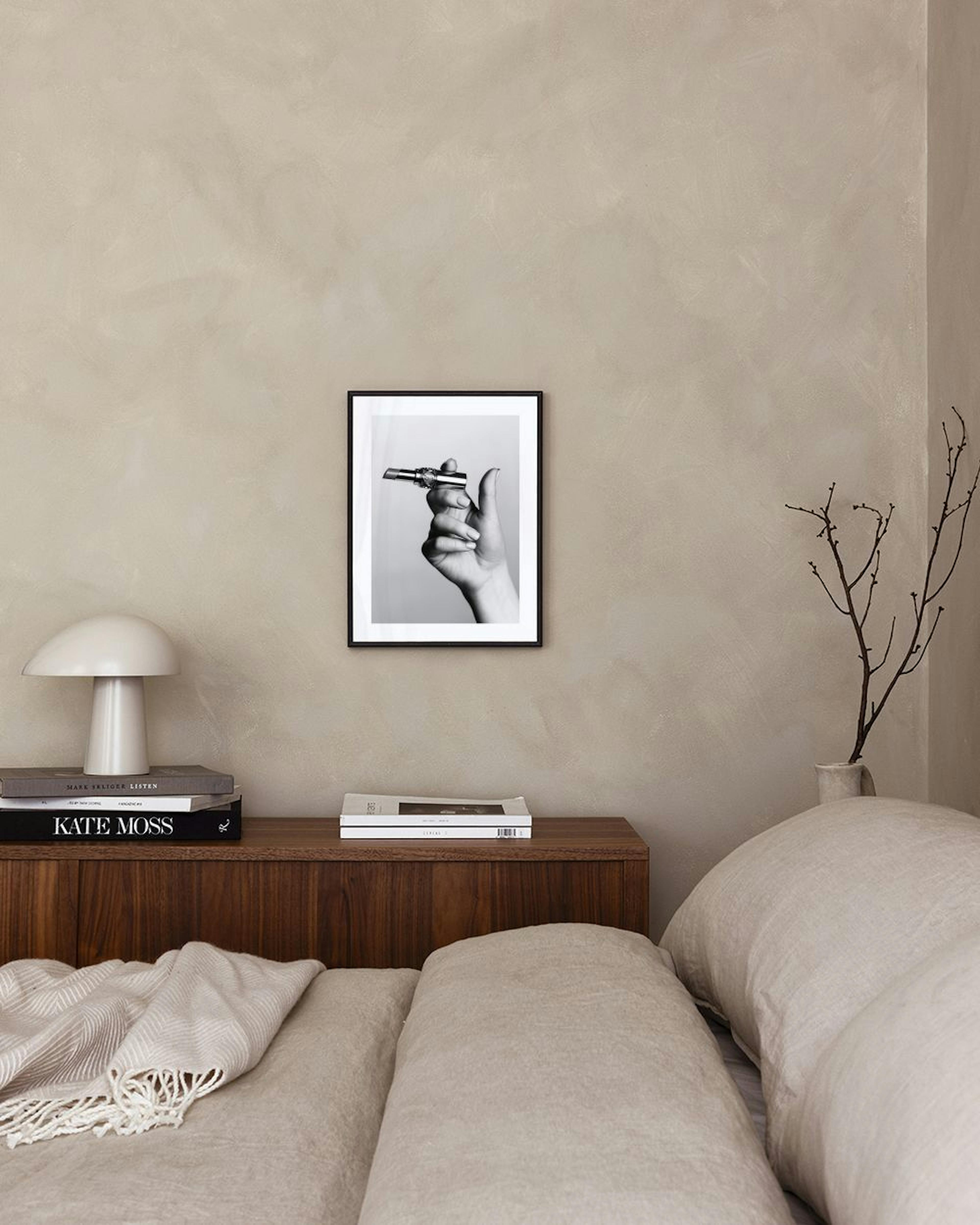 Schwarz-weiß Fotografie einer Hand, die einen Lippenstift hält, hängt über einem Sideboard mit Büchern.