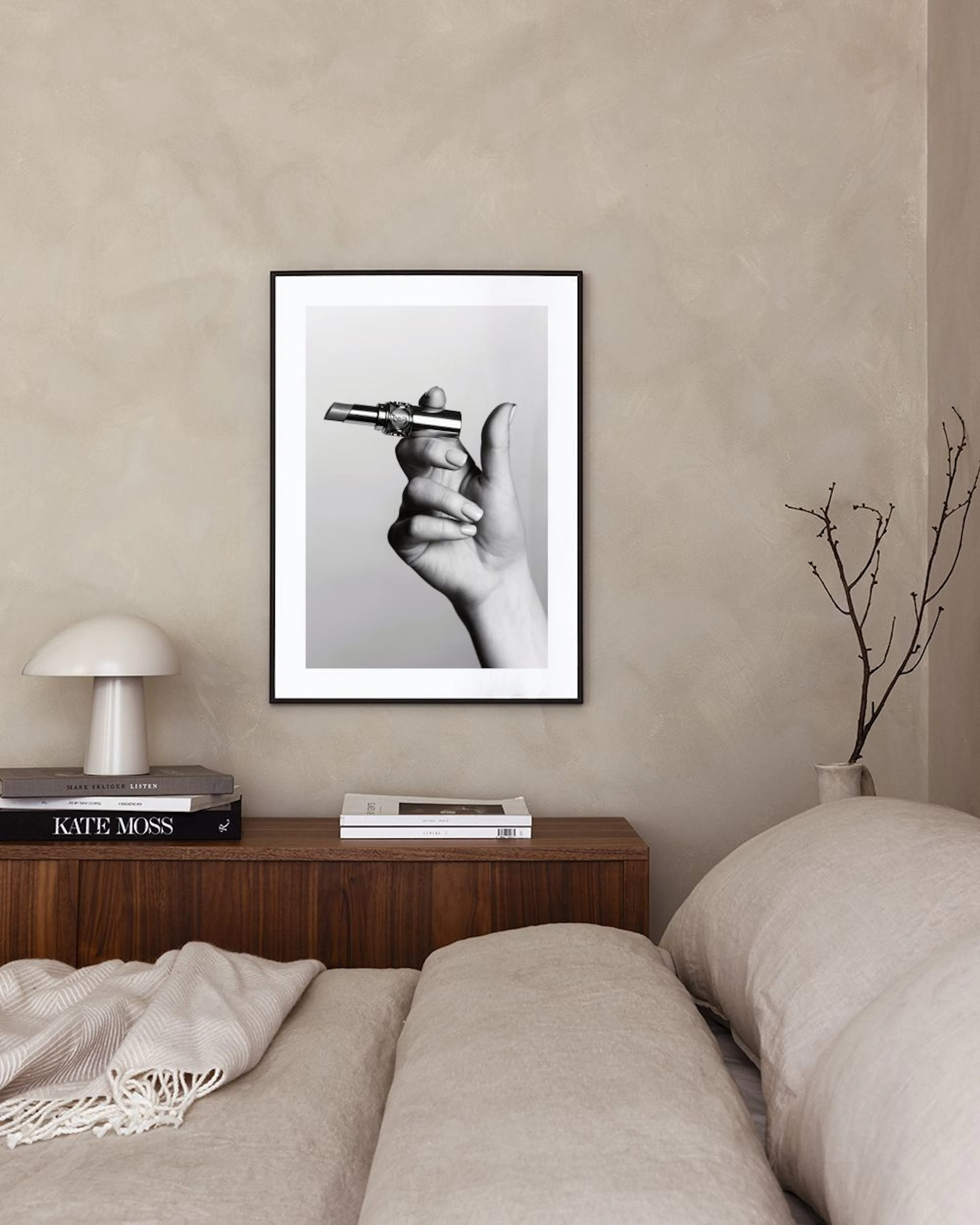 Black and white print of a hand holding a lipstick, displayed above a green scallop-patterned cabinet with books and decor.