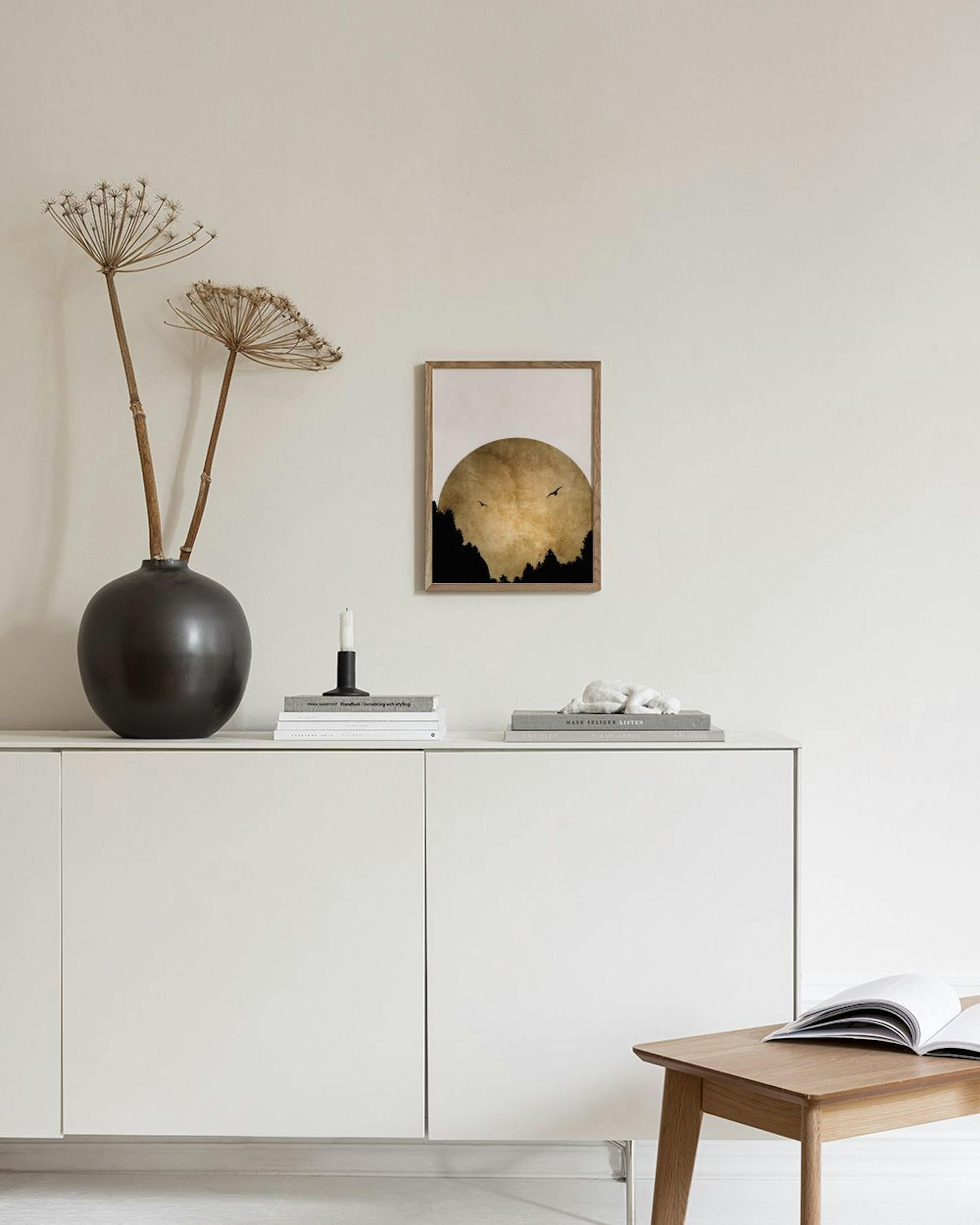 Affiche avec un soleil doré sur une forêt sombre, deux oiseaux en vol, accrochée au-dessus dune étagère blanche dans un salon mo