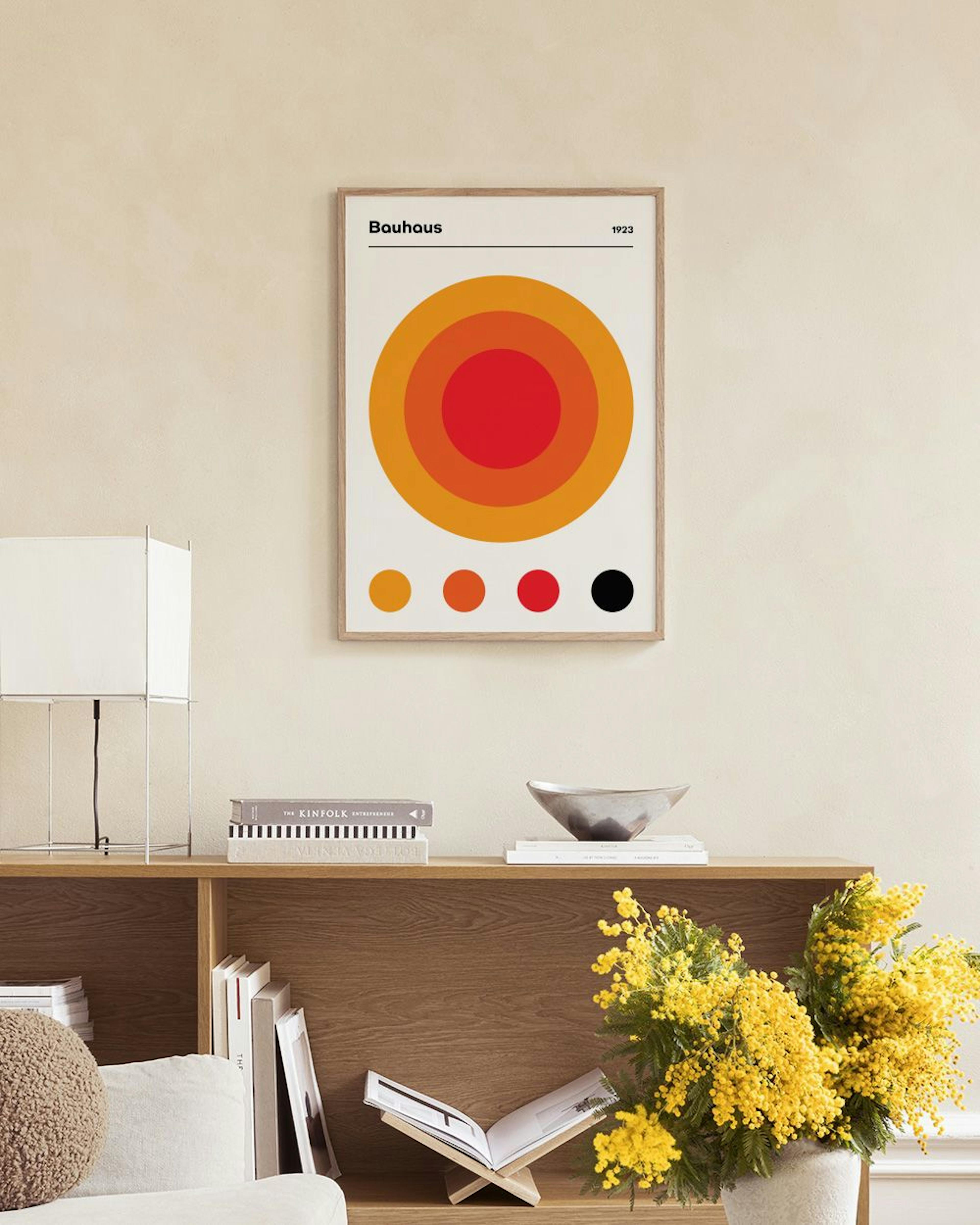 Plakat med Bauhaus-design av konsentriske sirkler i rød, oransje og gul, med fire fargeprøver under, henger over et marmorbord m