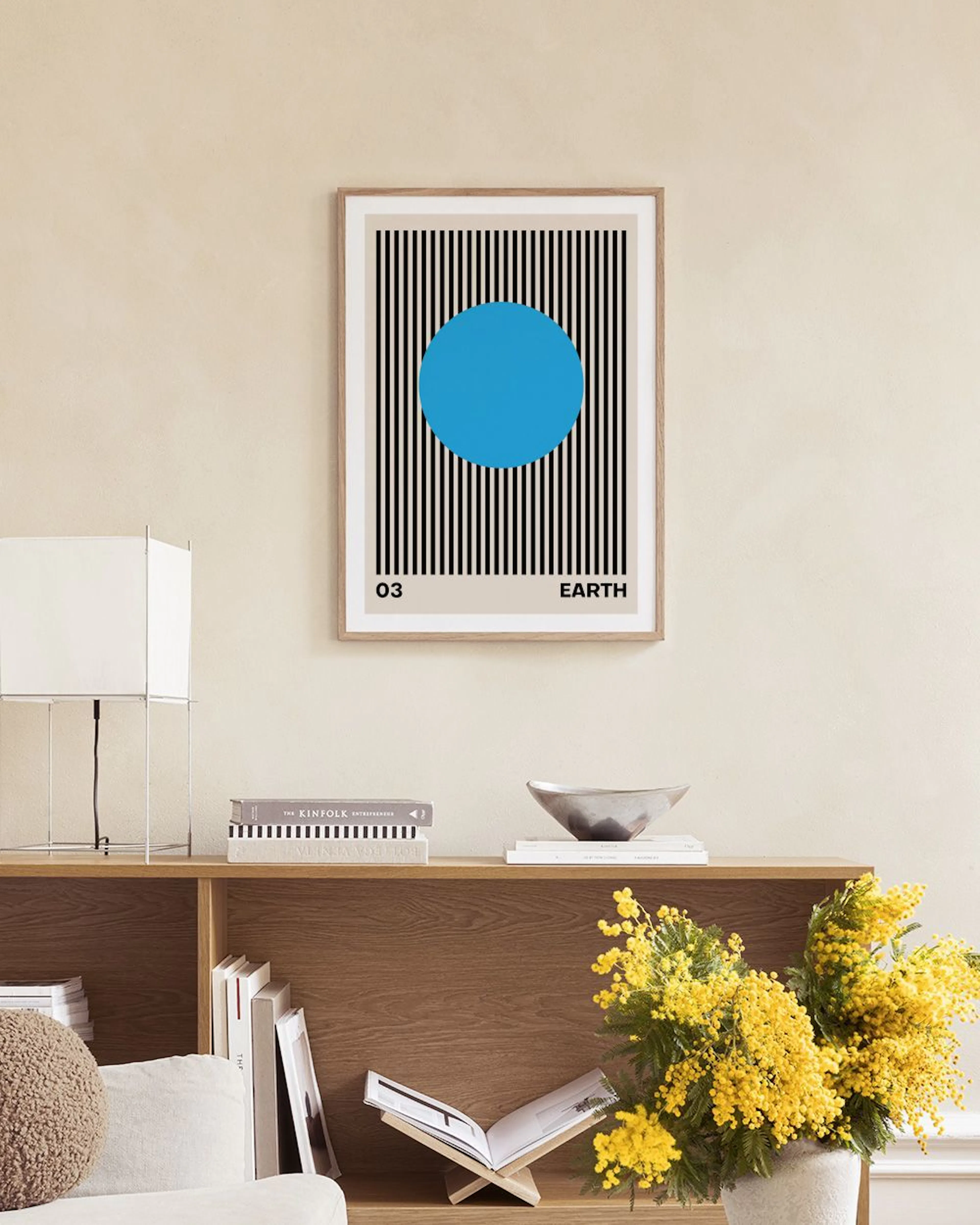 A print of a blue circle in a striped pattern, labeled Earth and 03, displayed on a grey shelf with decorative spheres and a whi