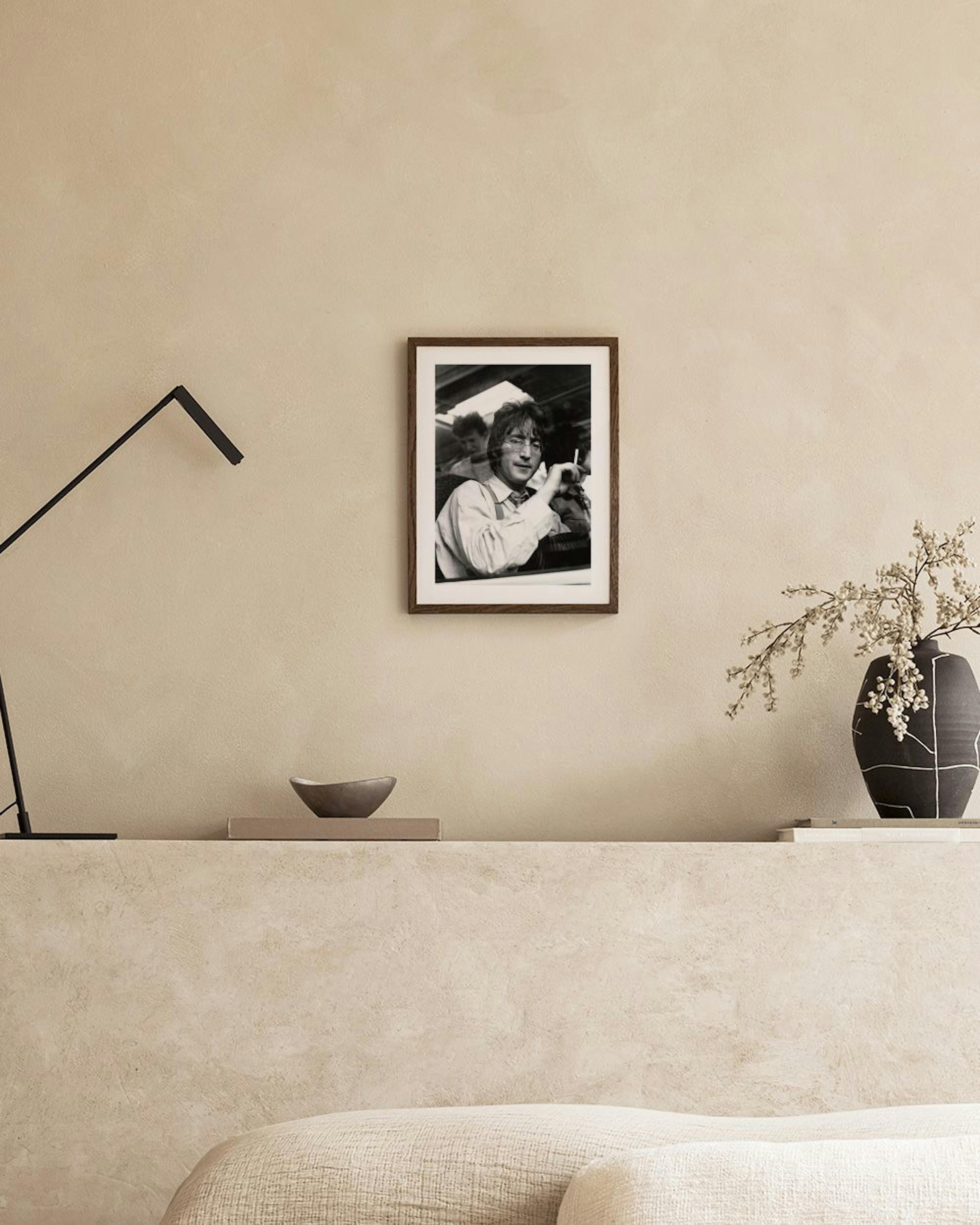 Poster in bianco e nero di John Lennon in unauto, con sigaretta, appeso sopra un libro, vasi e una sedia blu.