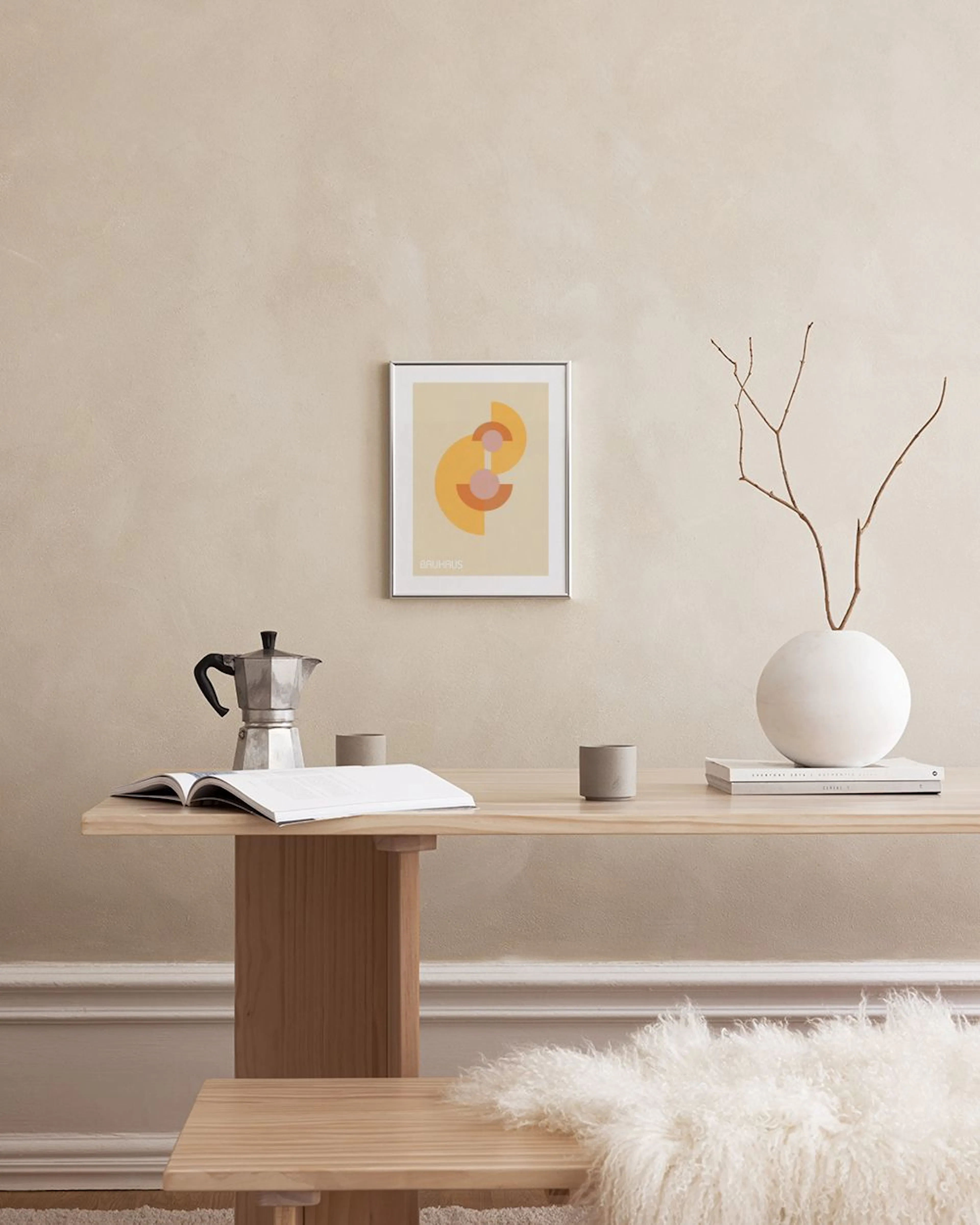 Een poster met Bauhaus-geïnspireerde geometrische vormen in geel, oranje en roze, hangend boven een zwarte plank met een grijze 